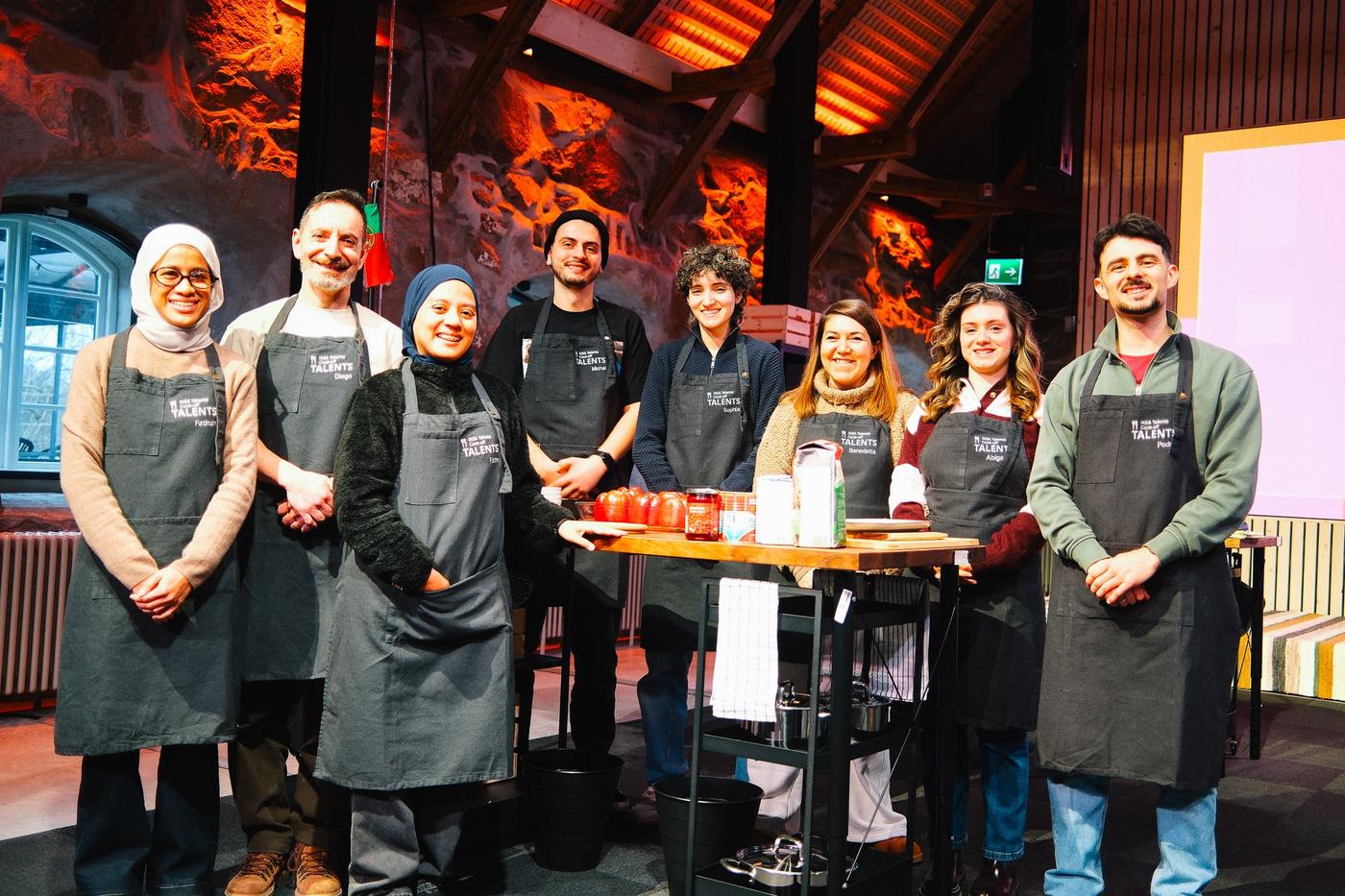 A group of people wearing aprons, standing by a table with cooking ingredients.