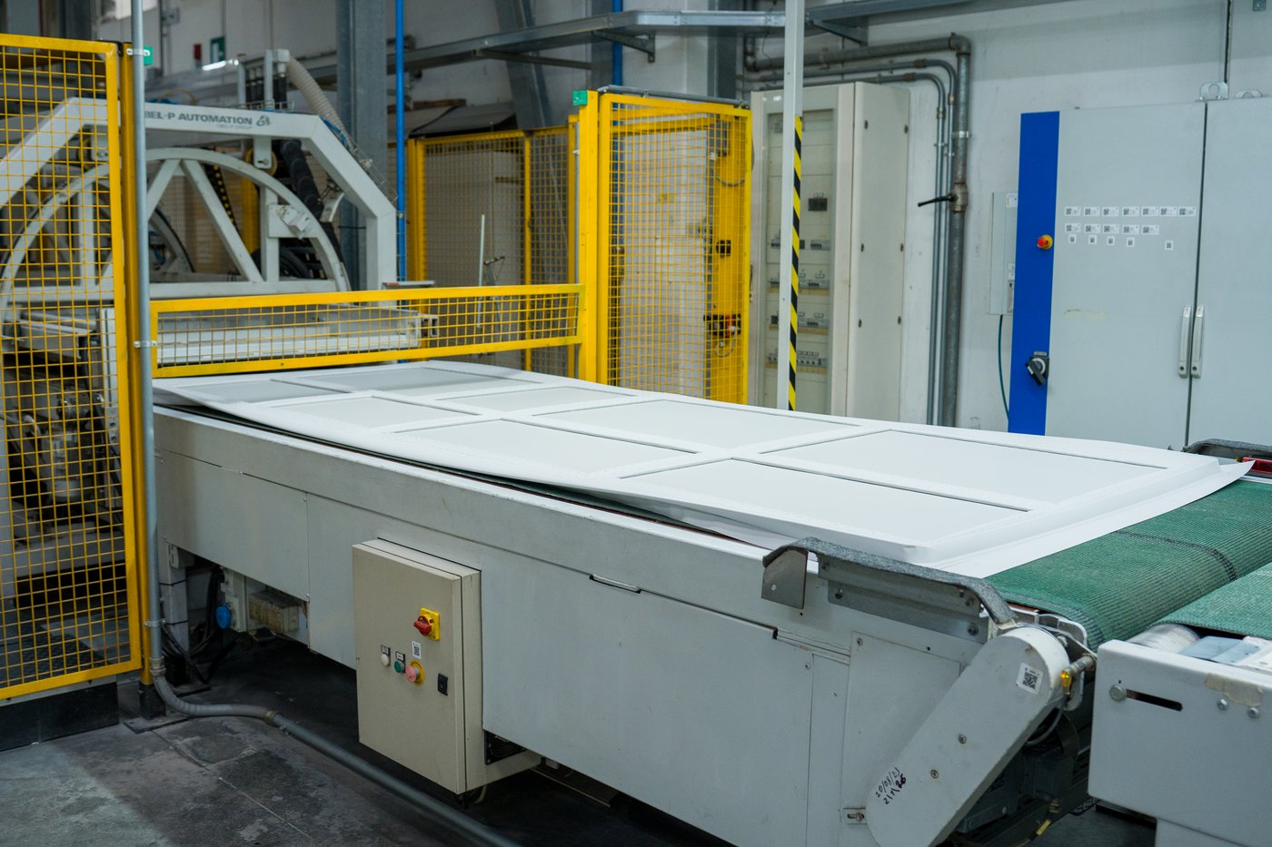 A length of uncut kitchen fronts covered in a foil laminate on a conveyor belt.