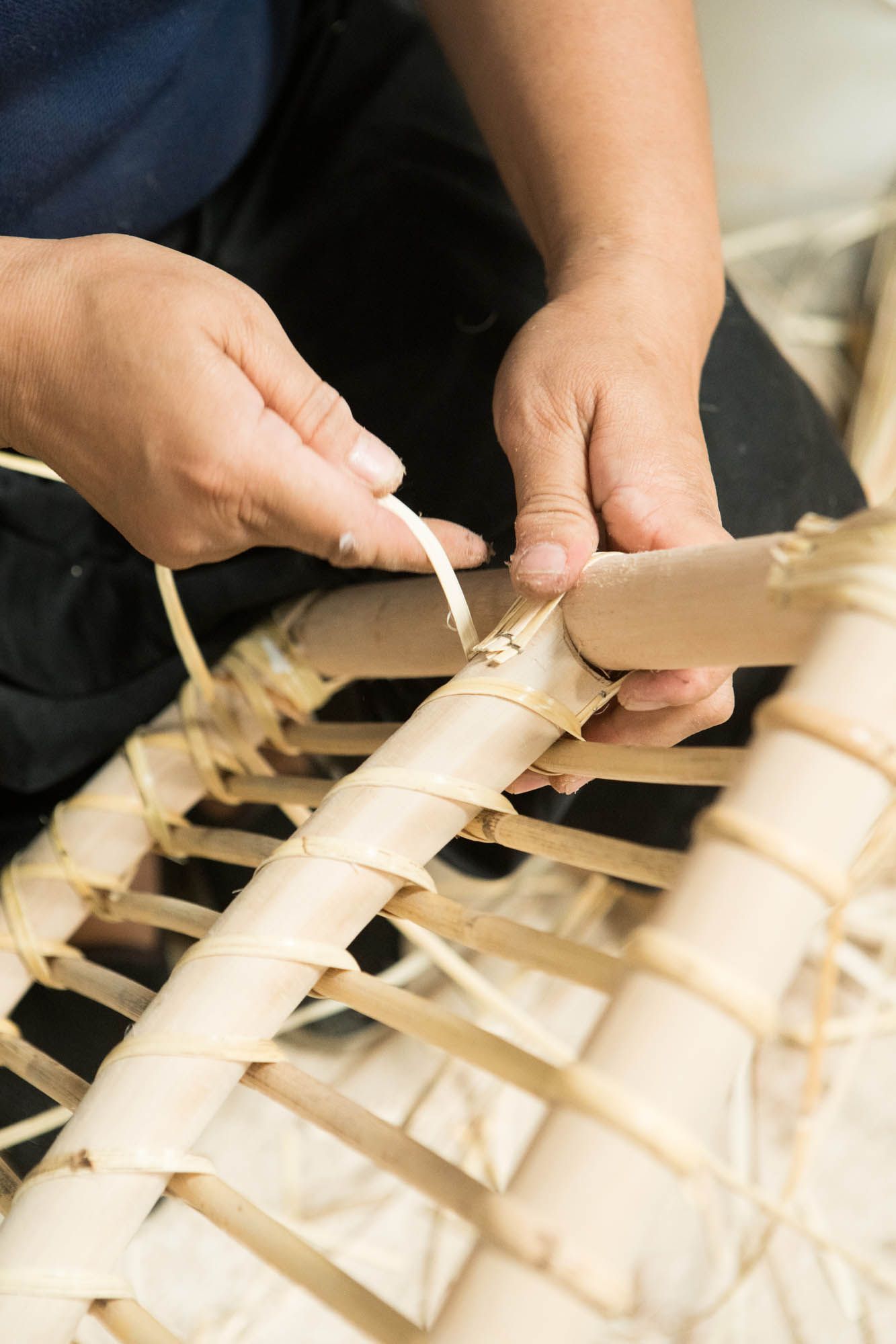 Hands weaving rattan fibres onto a rattan cane frame.