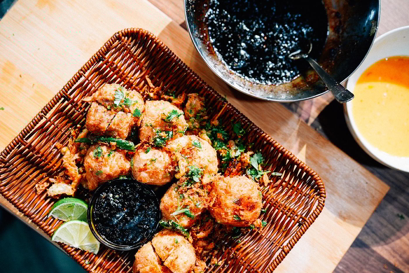A woven tray filled with golden, crispy stuffed fried tofu, accompanied by lime wedges and a small bowl of sambal soy sauce. Nearby, a larger bowl contains sauce and a spoon, creating an appetising display.
