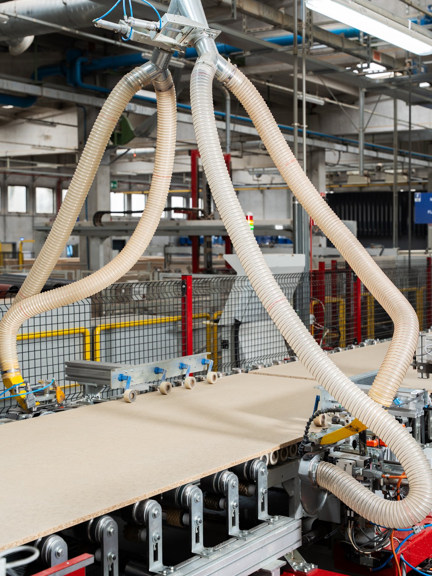 A factory setting with large tubes connected to the edge of a conveyor belt where MDF pieces roll along.