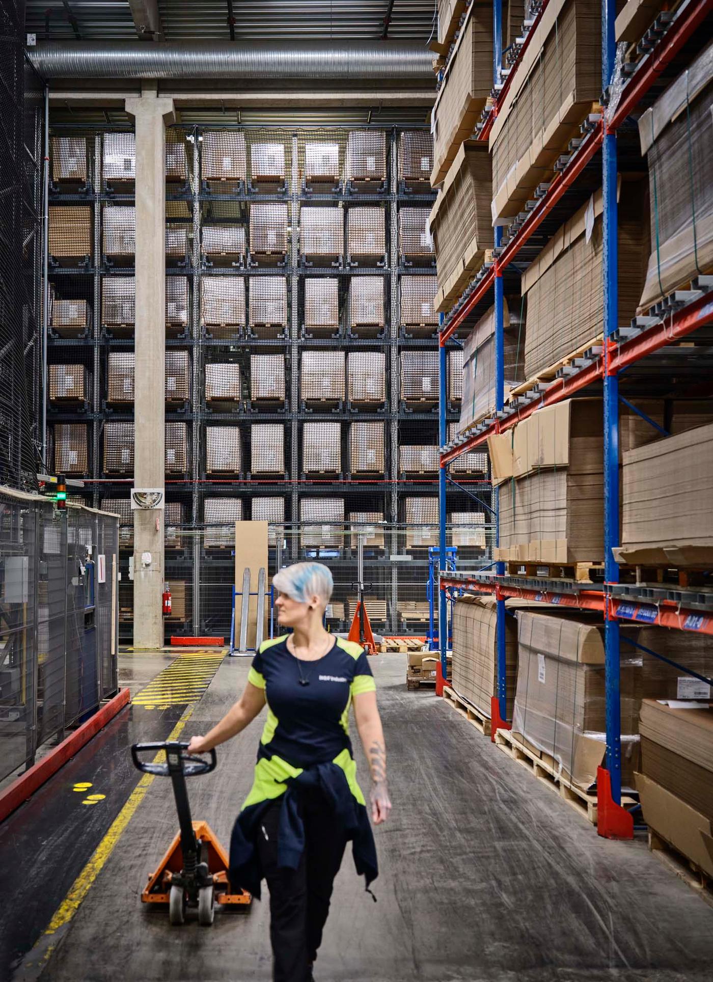 A person in a warehouse setting, wearing safety gear and pulling a pallet jack.