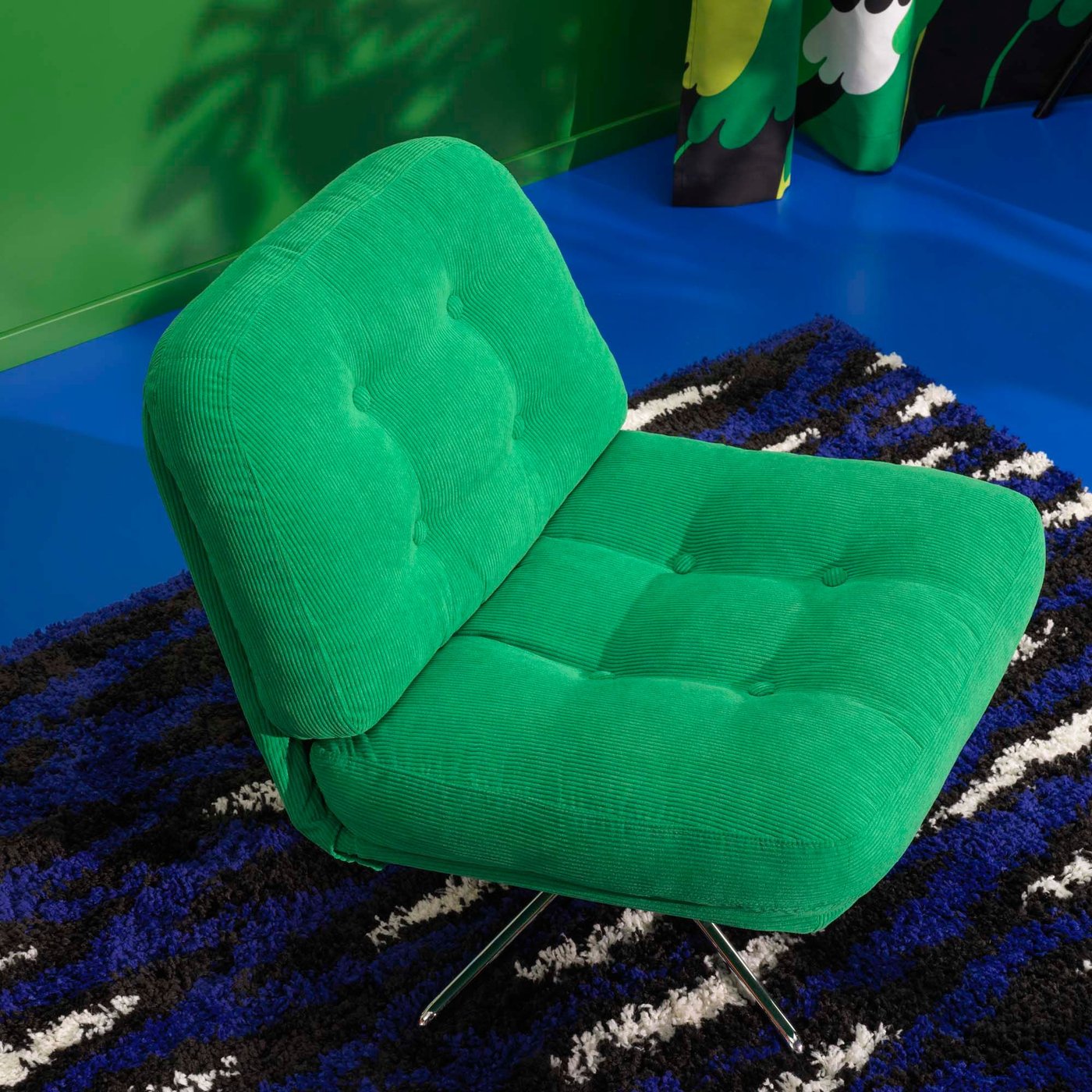 A green DYVLINGE swivel chair is placed on a blue, black and white rug, against a blue and green backdrop.