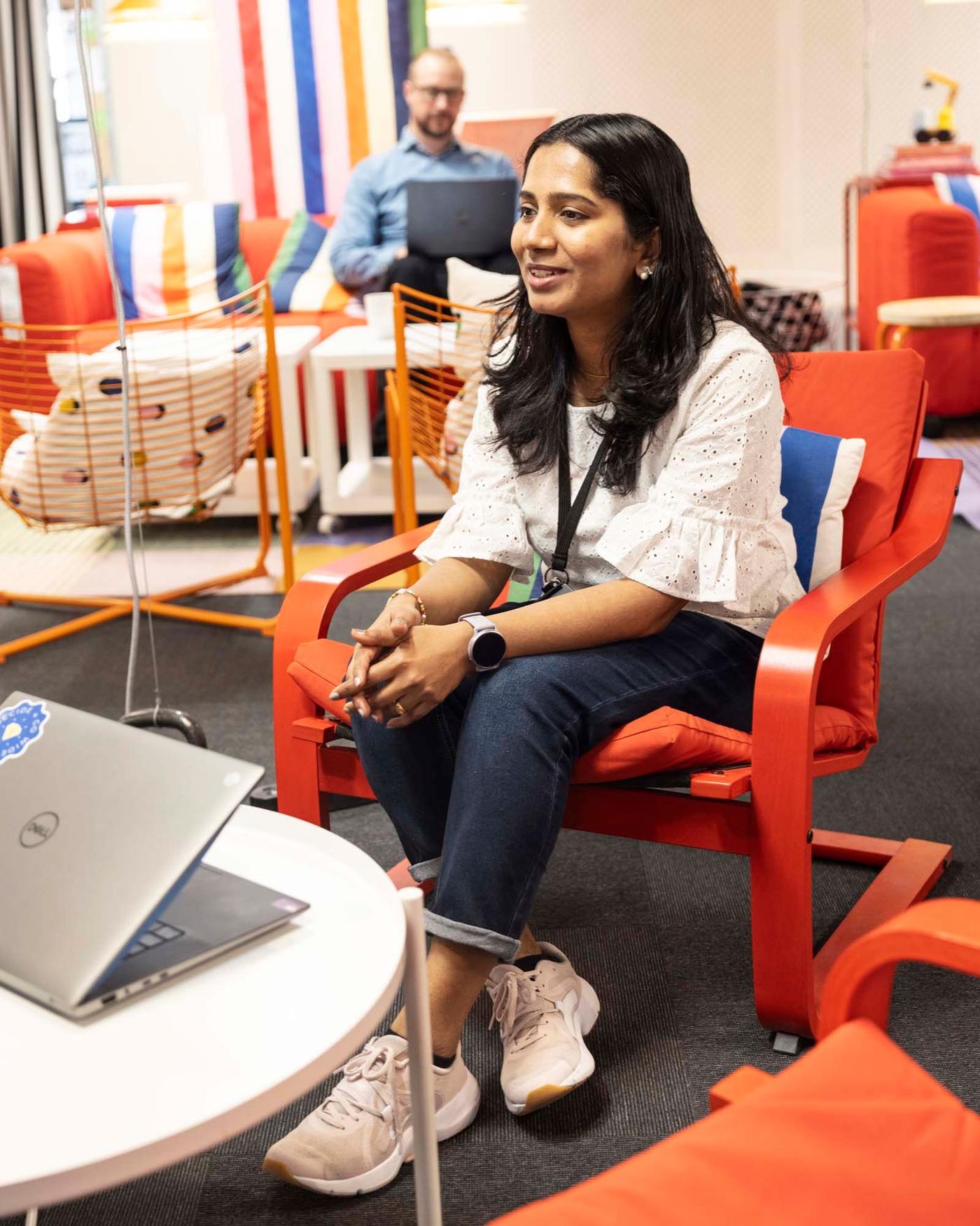 A person sitting in an armchair with a laptop on a white coffee table in front of her.
