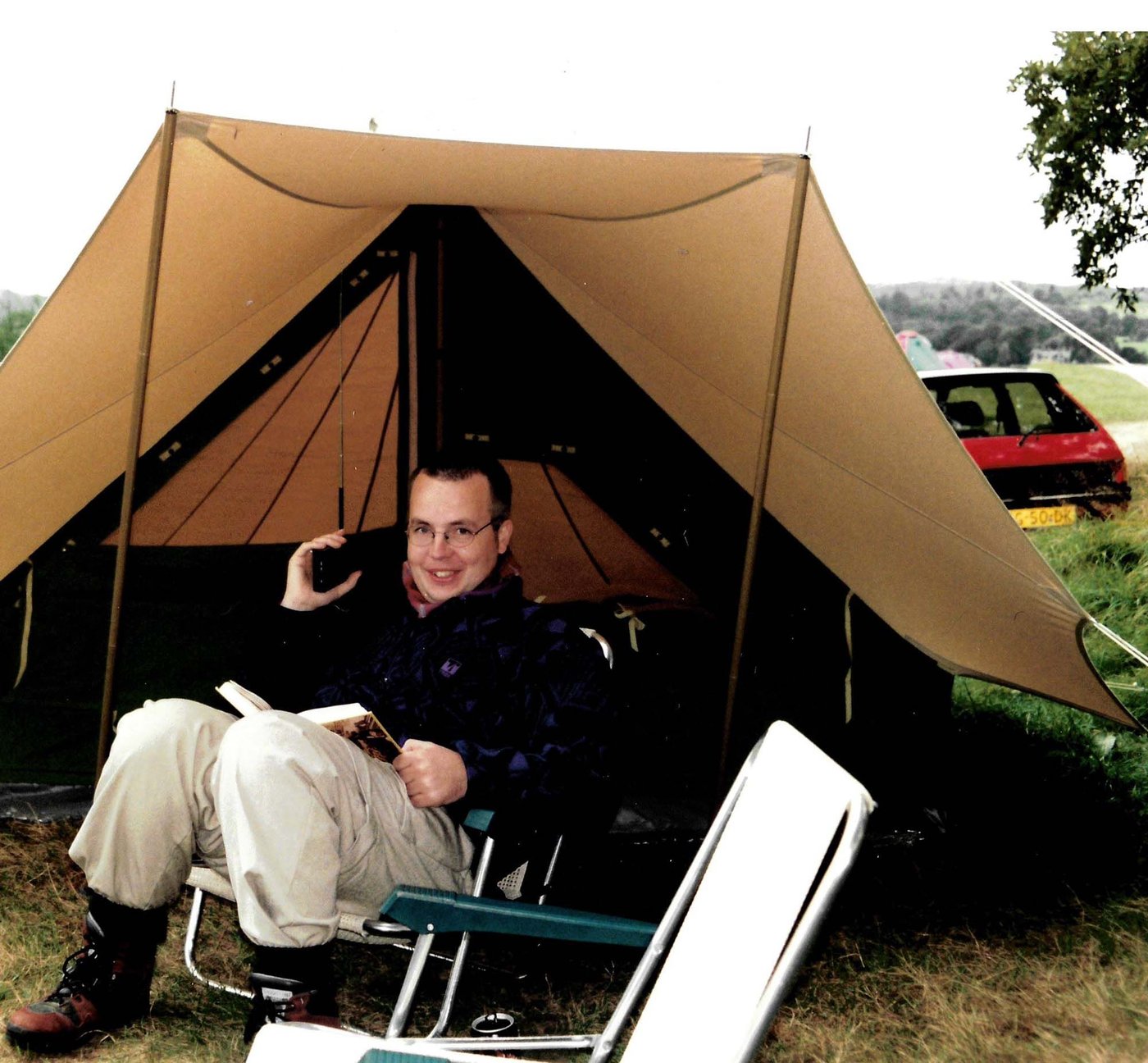 IKEA co-worker Erik sits on a chair in a tent outside. He has a book on his lap and he is smiling.