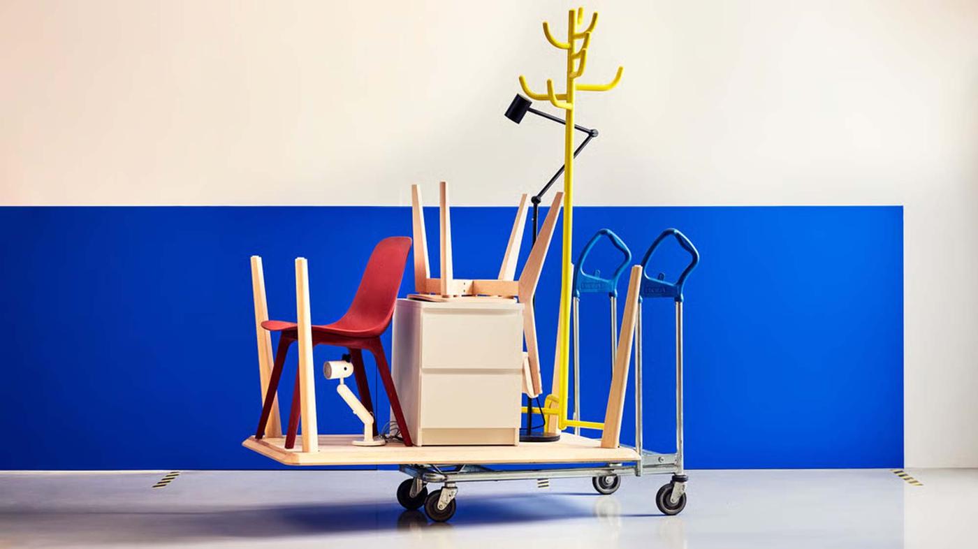 A flat cart with IKEA furniture assembled on top with a blue wall behind it.