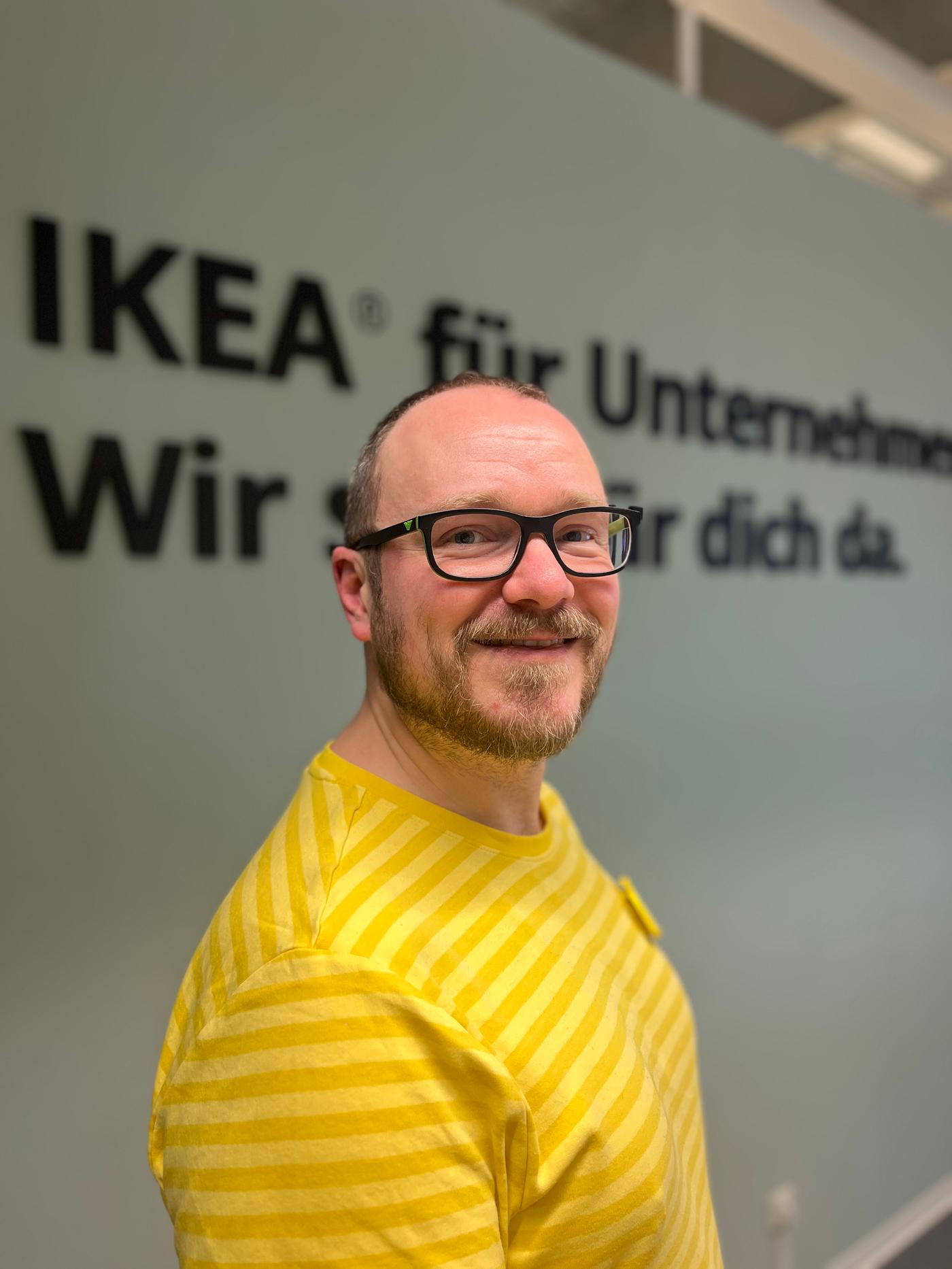 IKEA Germany co-worker Frank smiles at the camera, as he stands in front of a sign.