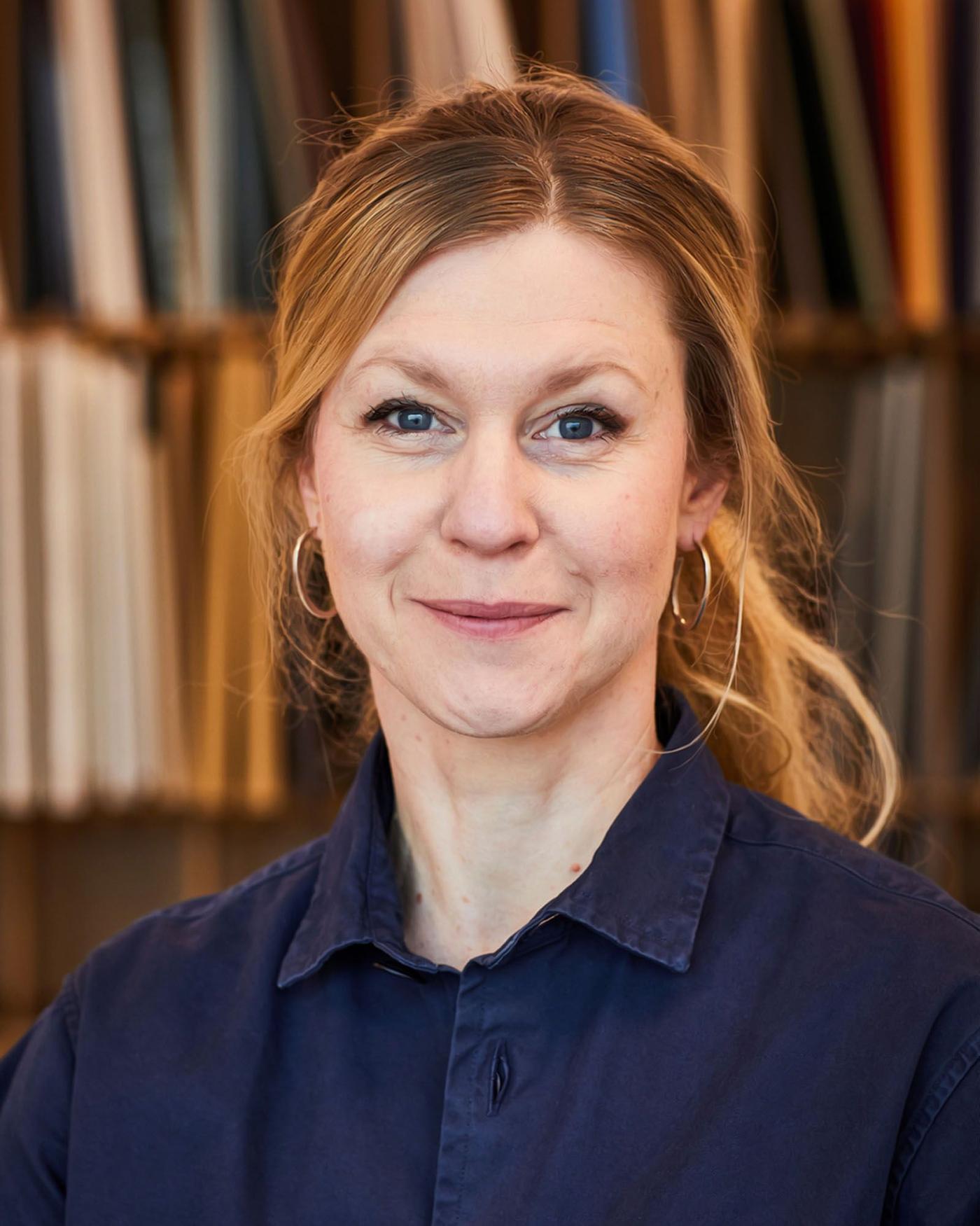 Portrait of Fredrika Inger, wearing a dark blue shirt and with a large bookshelf in the background.