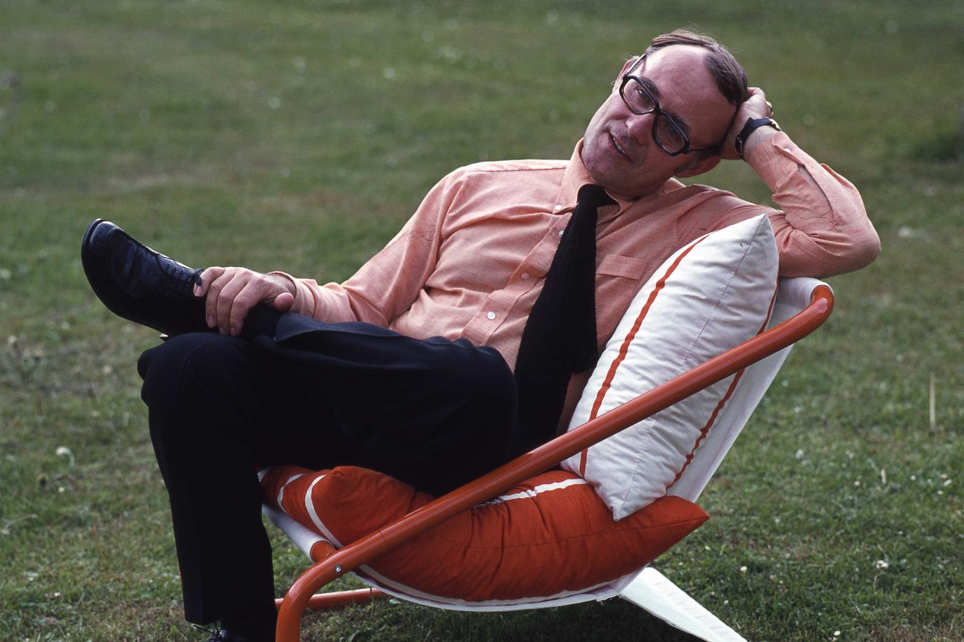 Ingvar Kamprad sits on a red and white chair outside on a grass surface.