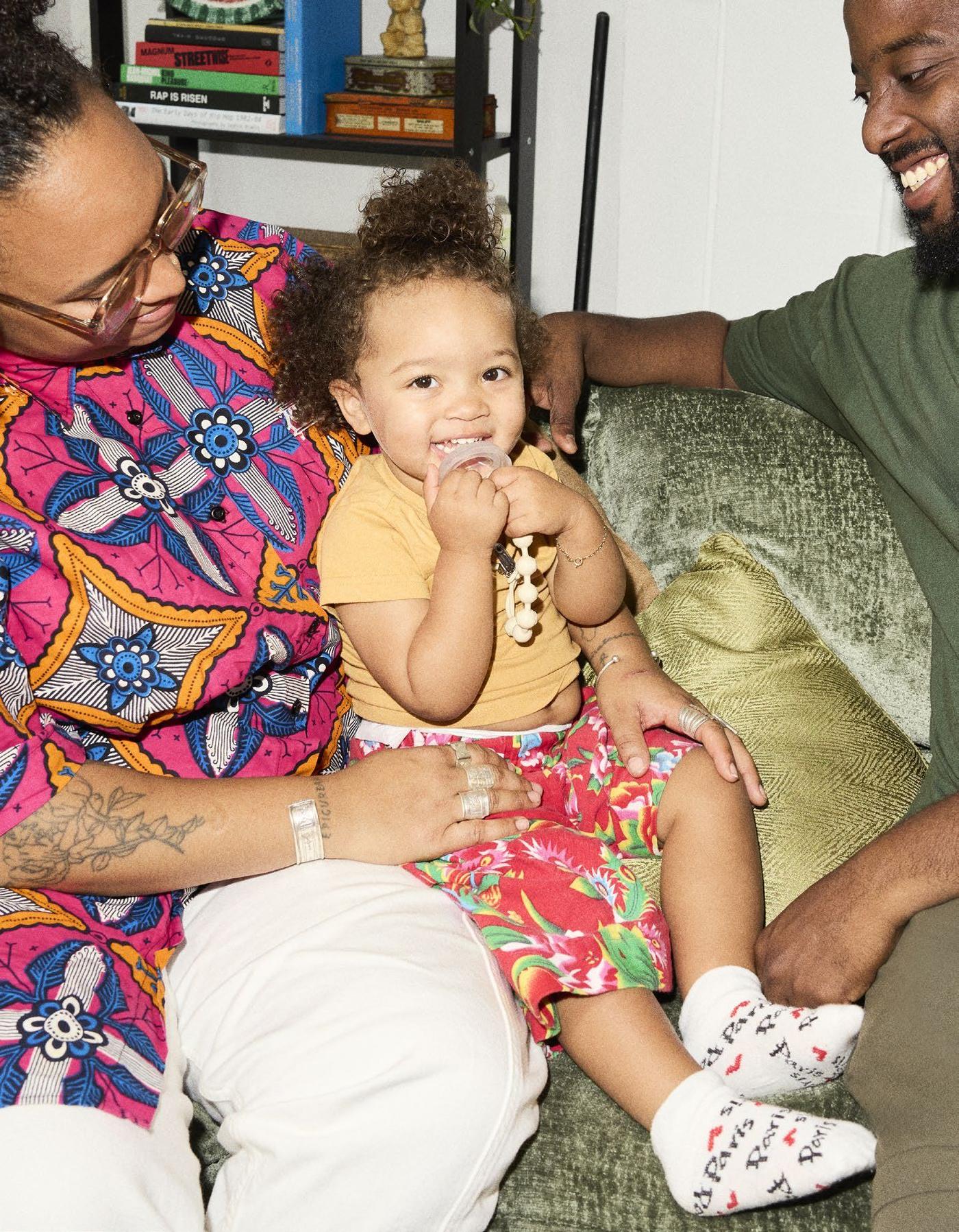 Estelle and her husband sit and look at their child, sitting on Estelle's lap. They all smile.