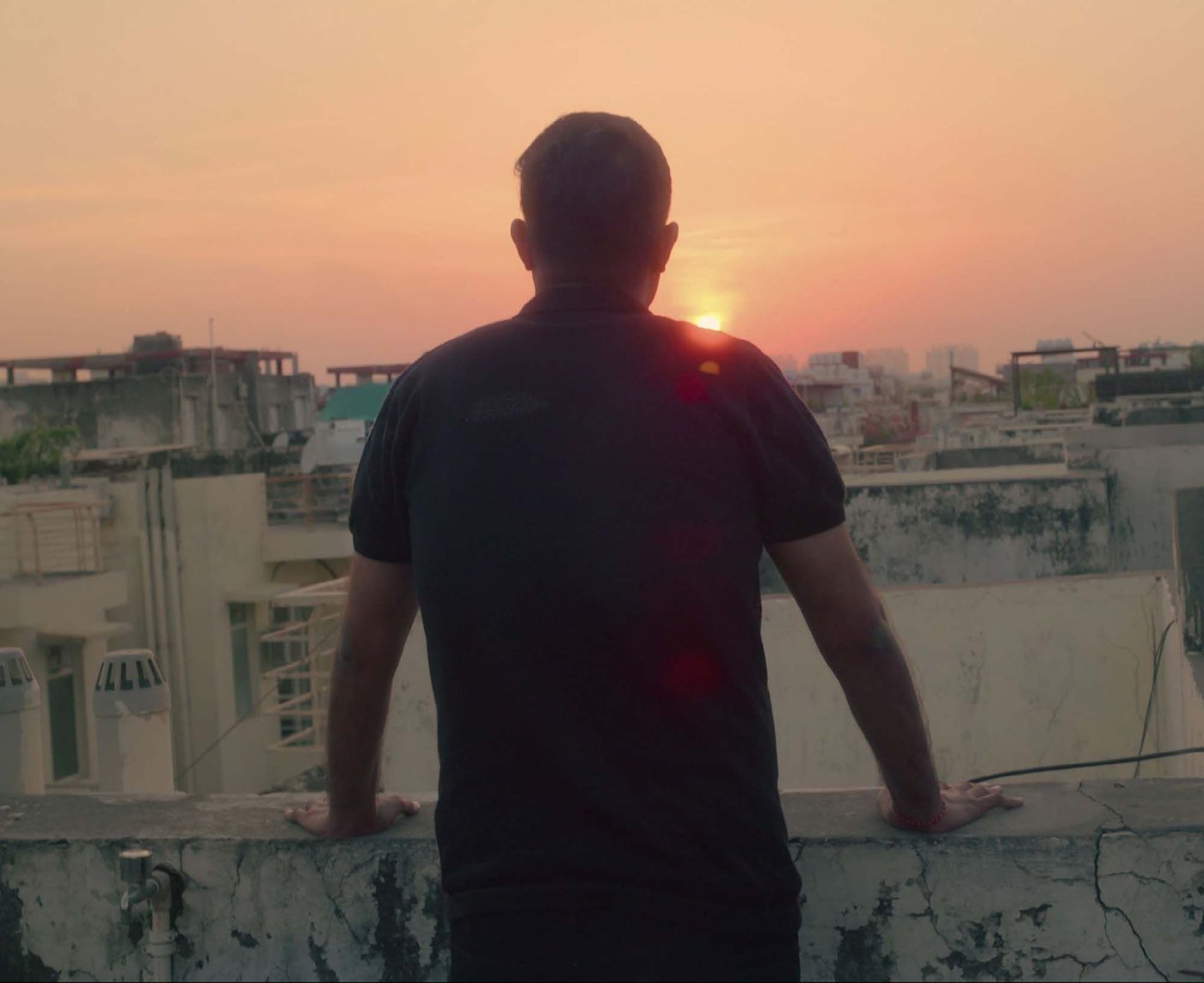 The silhouette of the back of a person looking out over a city landscape at sunset.