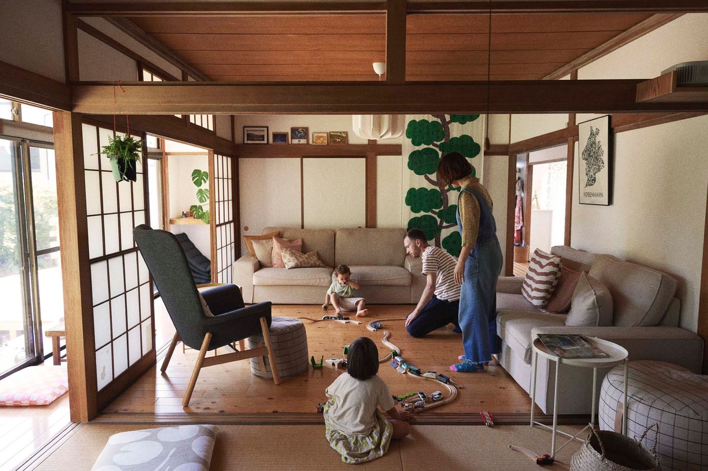 A family plays with a toy train set on the floor of a living room.
