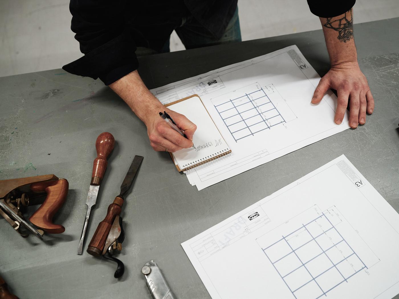 A pair of hands on a design drawing. One hand is writing notes on a note pad.
