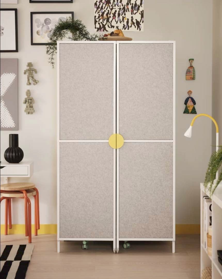 A grey cabinet from the BRÄNNBOLL gaming collection stands against a wall. it is surrounded by pictures and furniture.