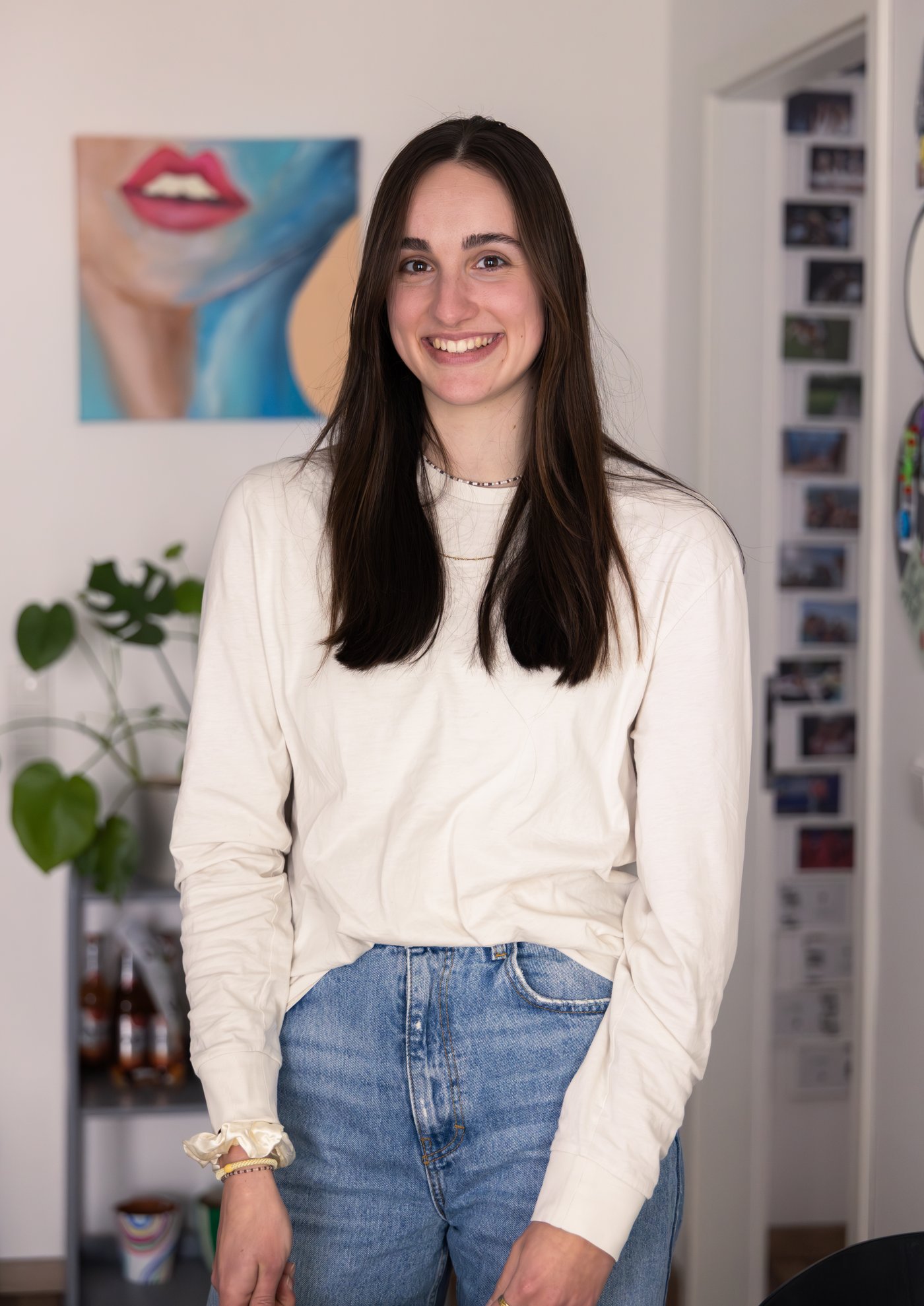 A portrait of Gina wearing a long-sleeved white top and blue jeans.