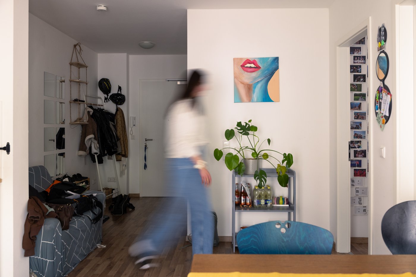 A blurred person walks through a white and blue living area with art, mirrors and photographs on the wall.