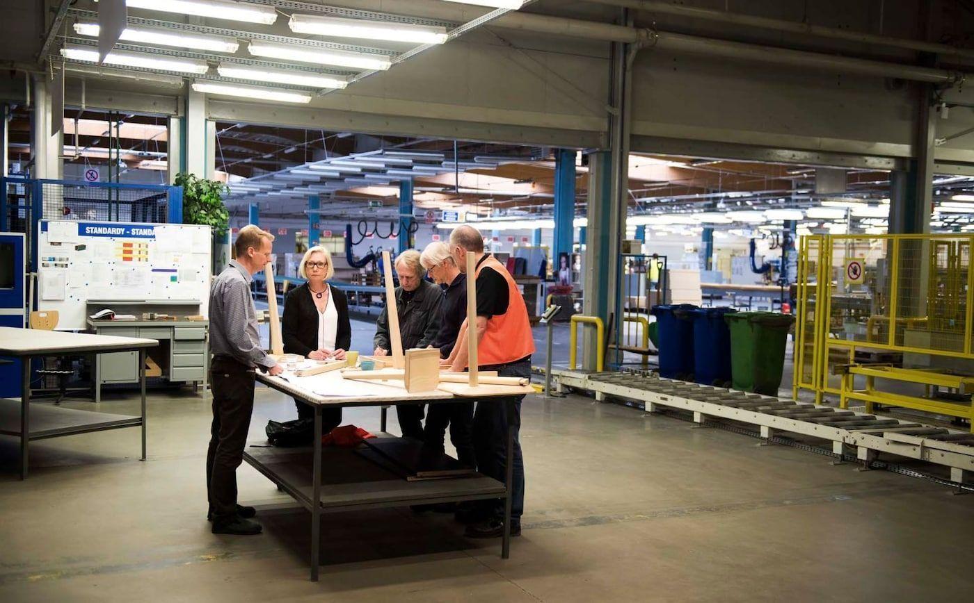 Designers and engineers look at sketches and prototypes in a workshop.
