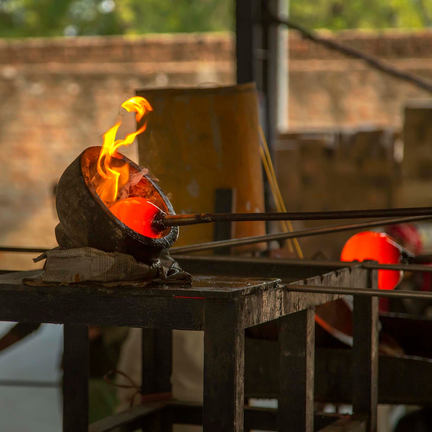 A gob of hot molten glass with flames, on the end of a metal pipe.