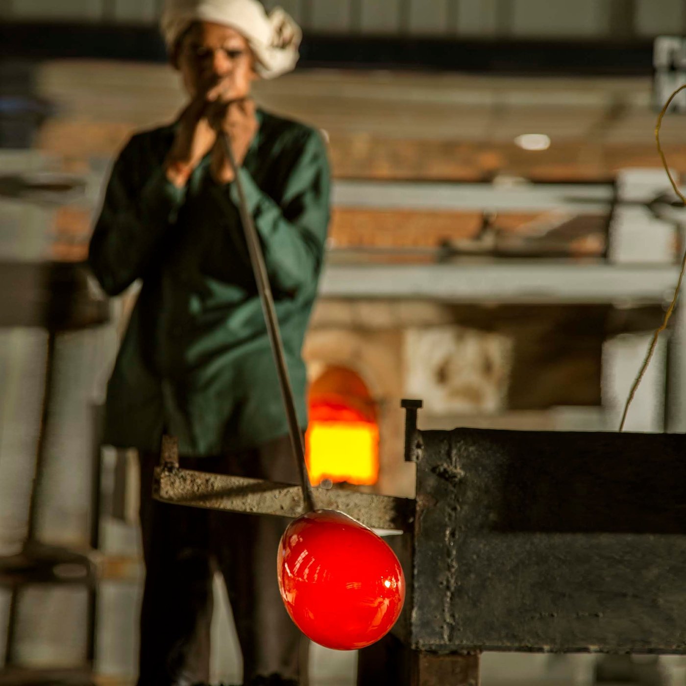 A person blows a glass HANGBJÖRK vase through a metal pipe.