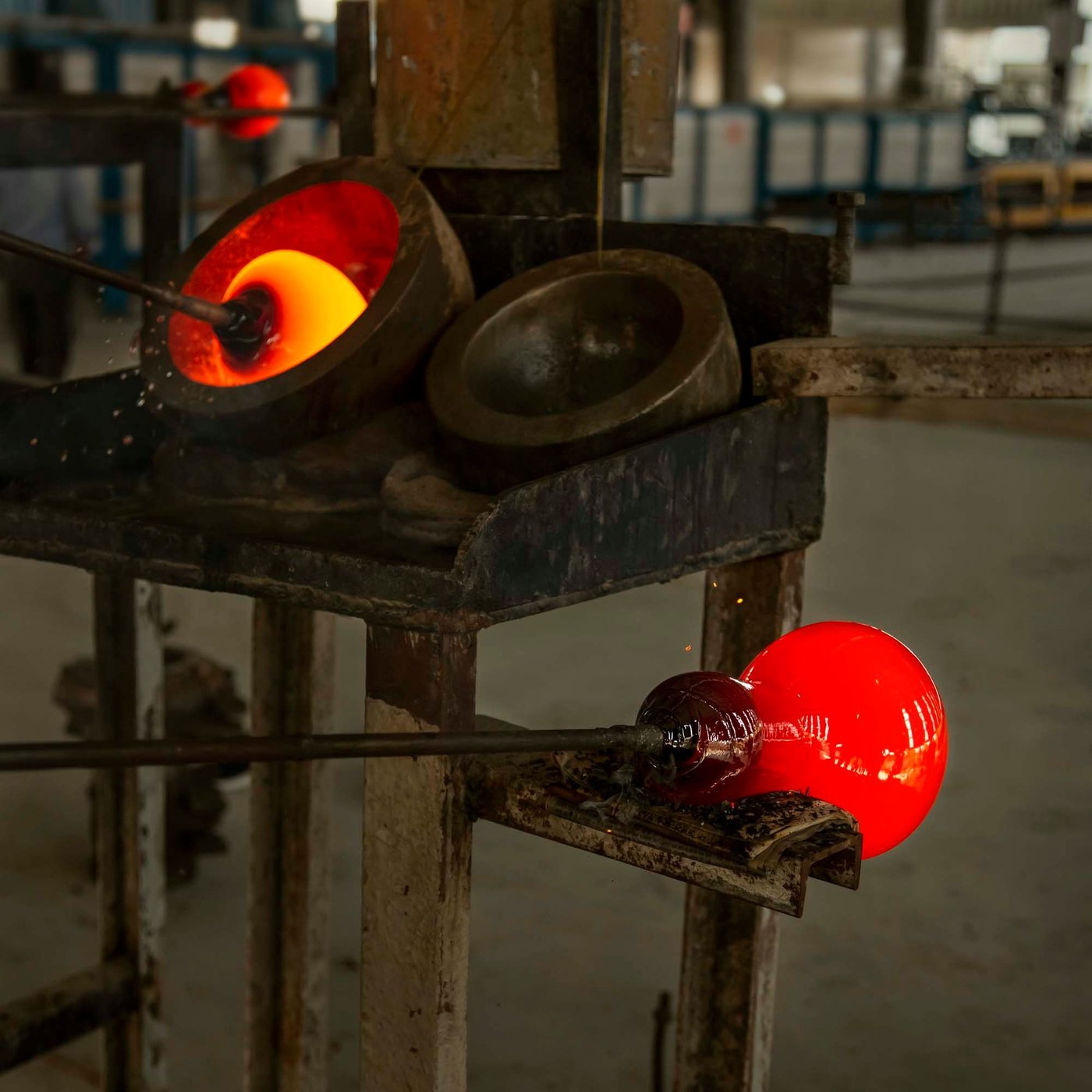 A gob of hot molten glass in a form, with a hot vase resting on a metal stand.