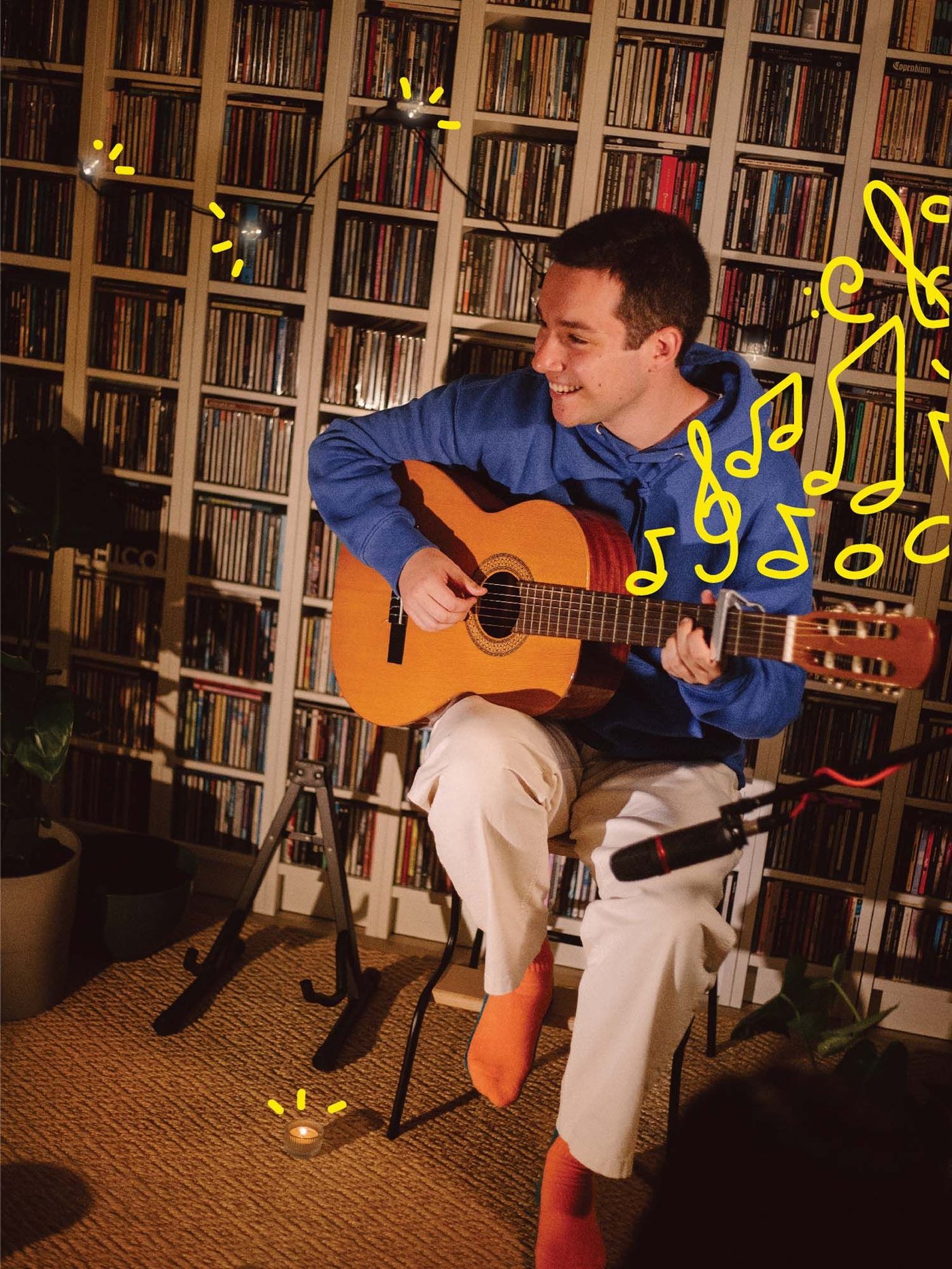 Lour sits on a stool in a dimly lit room playing his guitar.