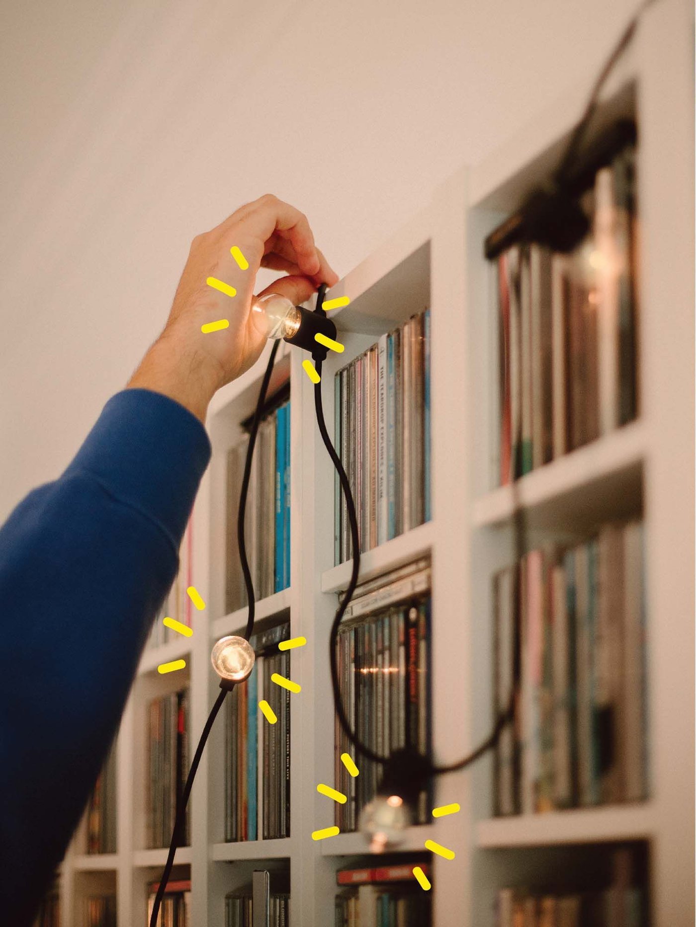 Lour hangs a string of lights across a bookshelf.