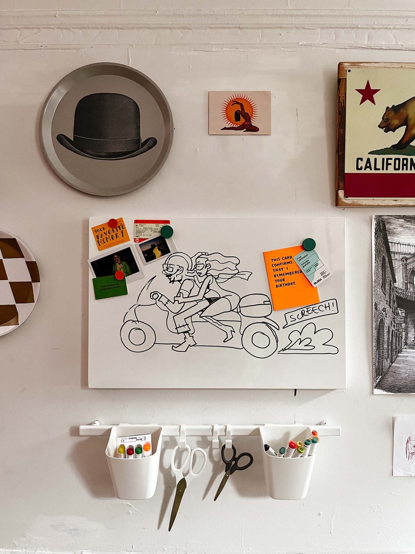 A wall with a memo board and art supplies in wall-mounted containers, surrounded by artwork and ornaments.