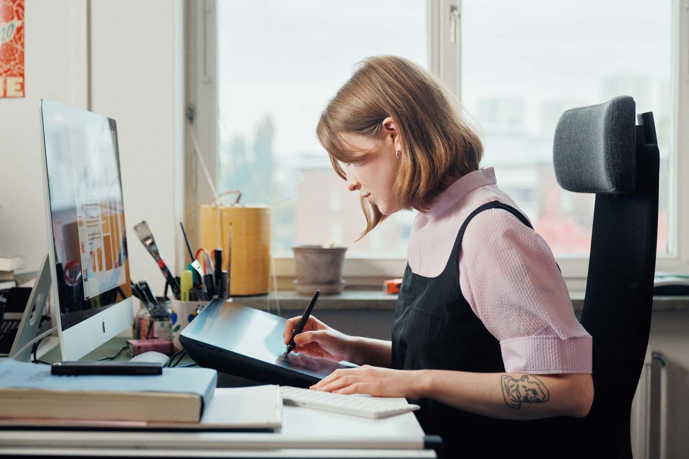 Designer Bim Eriksson sits at her desk, she is drawing on a digital tablet screen.