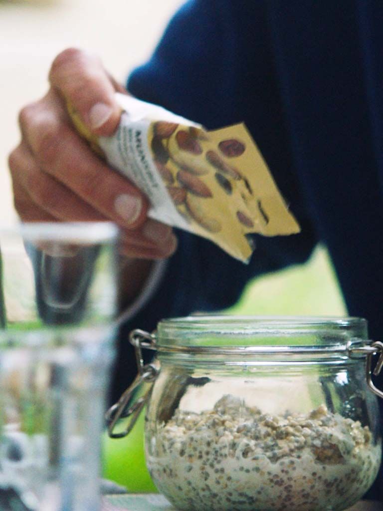 A screenshot of a hand pouring nuts into a jar of overnight oats.