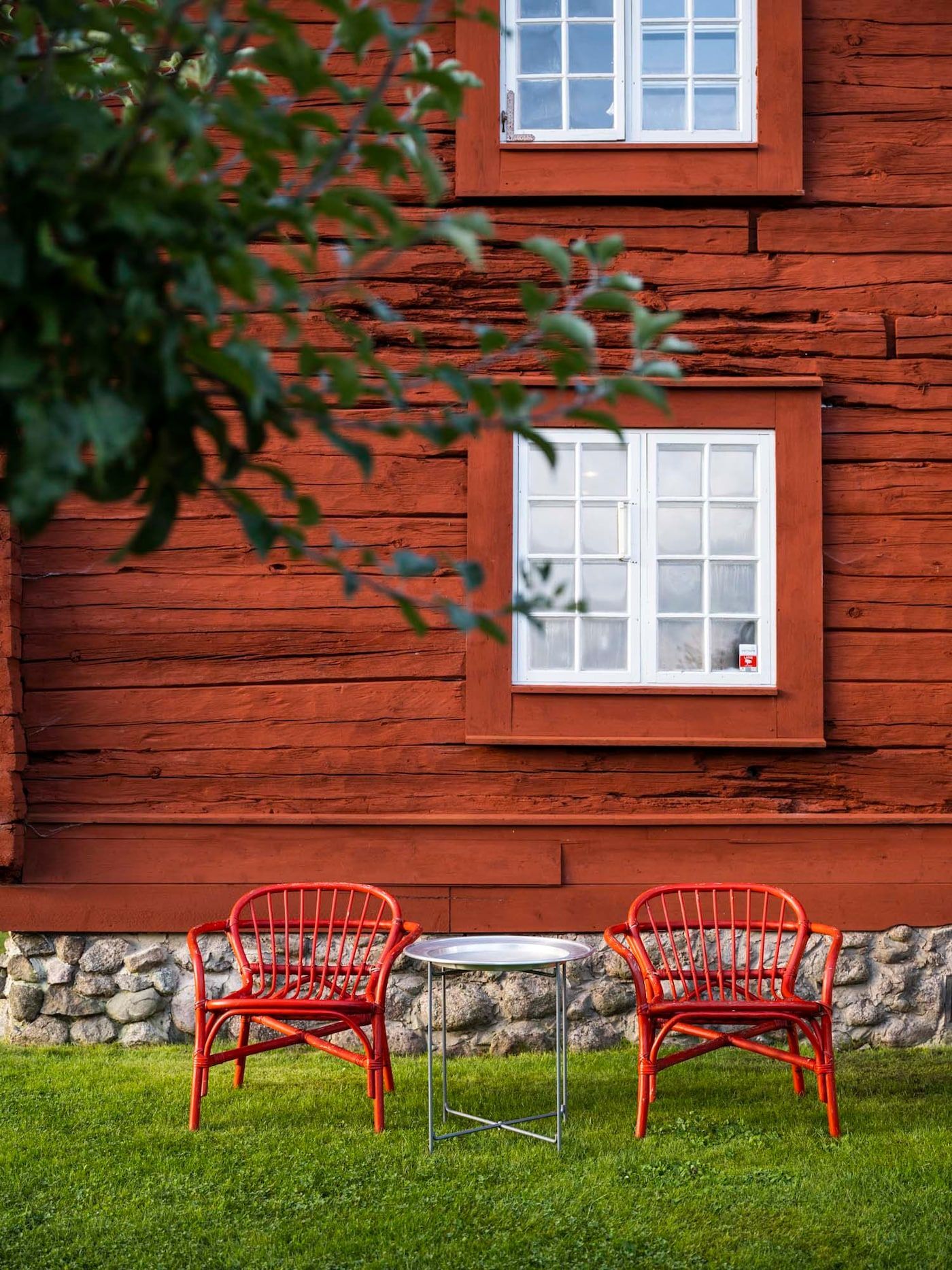 Two bright red outdoor chairs on a grassed area, with a Falu-red Swedish farmhouse behind.