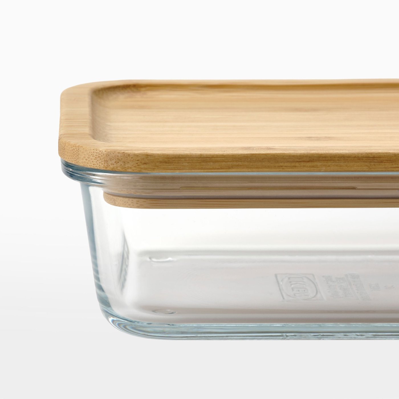 Close up of an empty one litre IKEA 365+ food container in clear glass with a bamboo lid on a light grey background.
