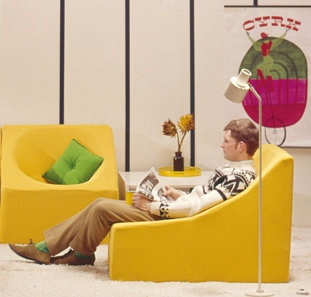 An old picture with a man sitting on a yellow sofa with a magazine