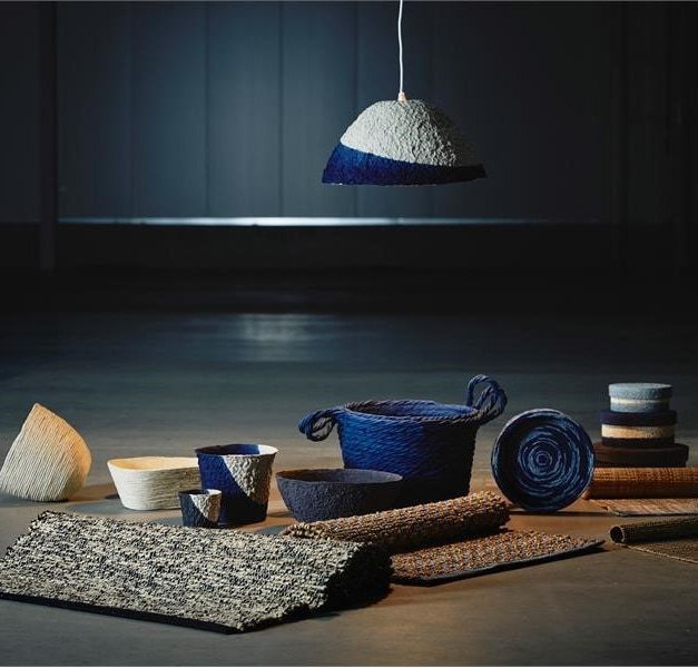 The IKEA FÖRÄNDRING collection of woven place mats and containers displayed on a dark grey surface.