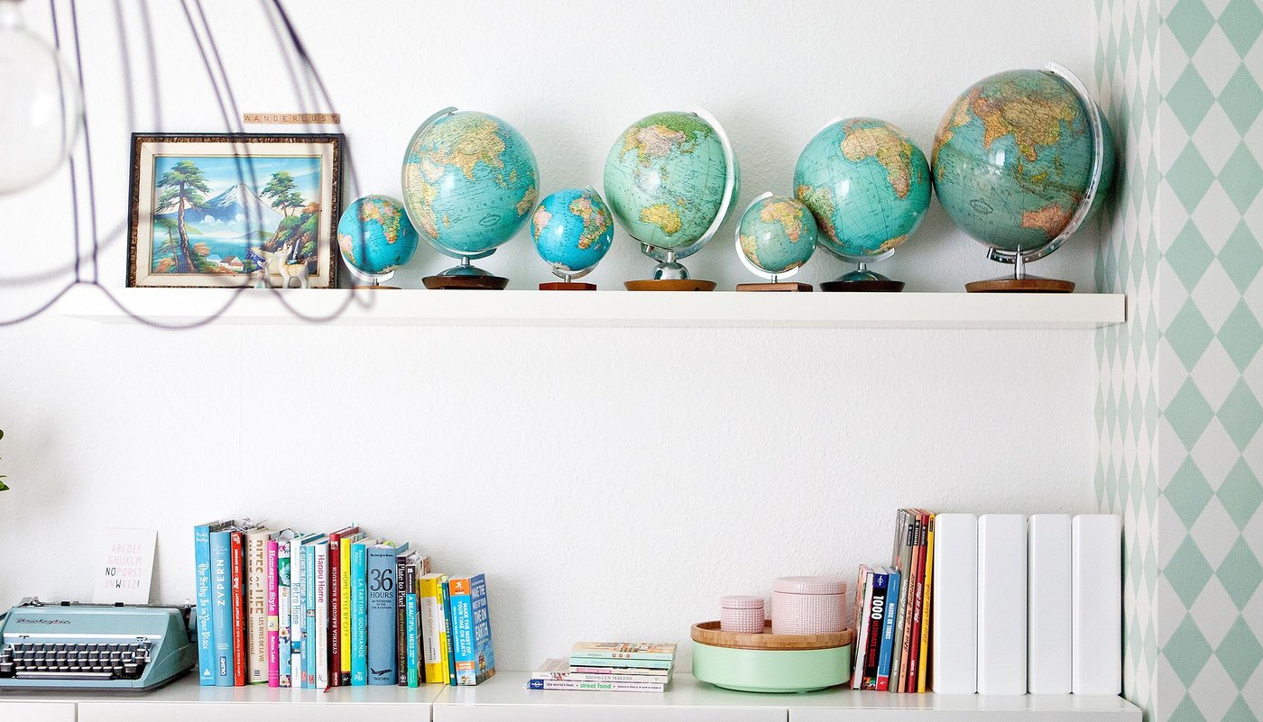 One white LACK wall shelf attached to a wall displaying items such as a series of globes in different sizes.