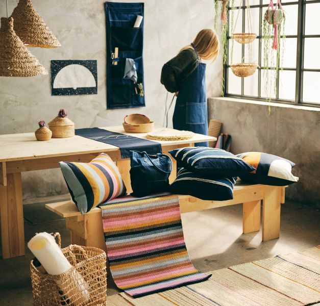 A woman standing next to a window putting on a denim apron.
