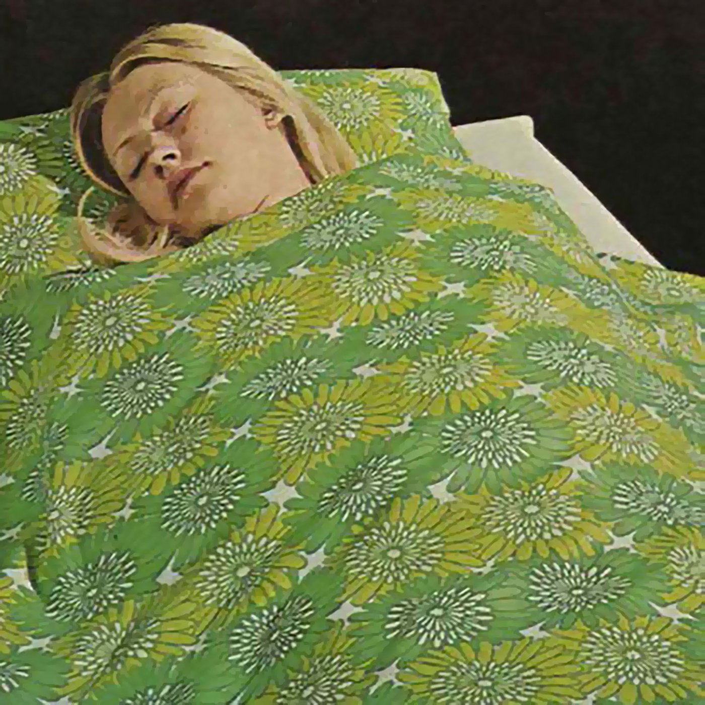A woman sleeps in a bed with green patterned bedlinen.