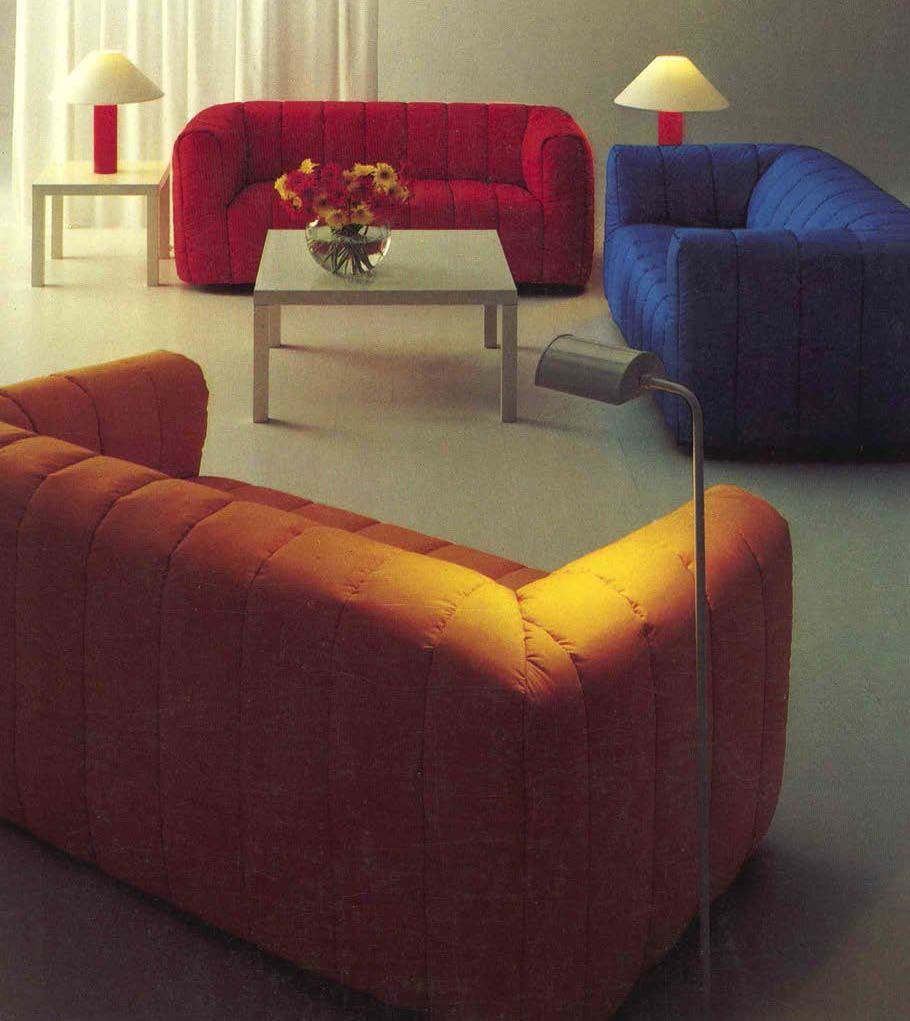 A yellow sofa, a red sofa and a blue sofa placed in a room alongside tables with lamps.