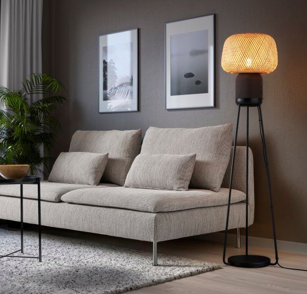 A lamp speaker standing on a tripod, next to a sofa. 