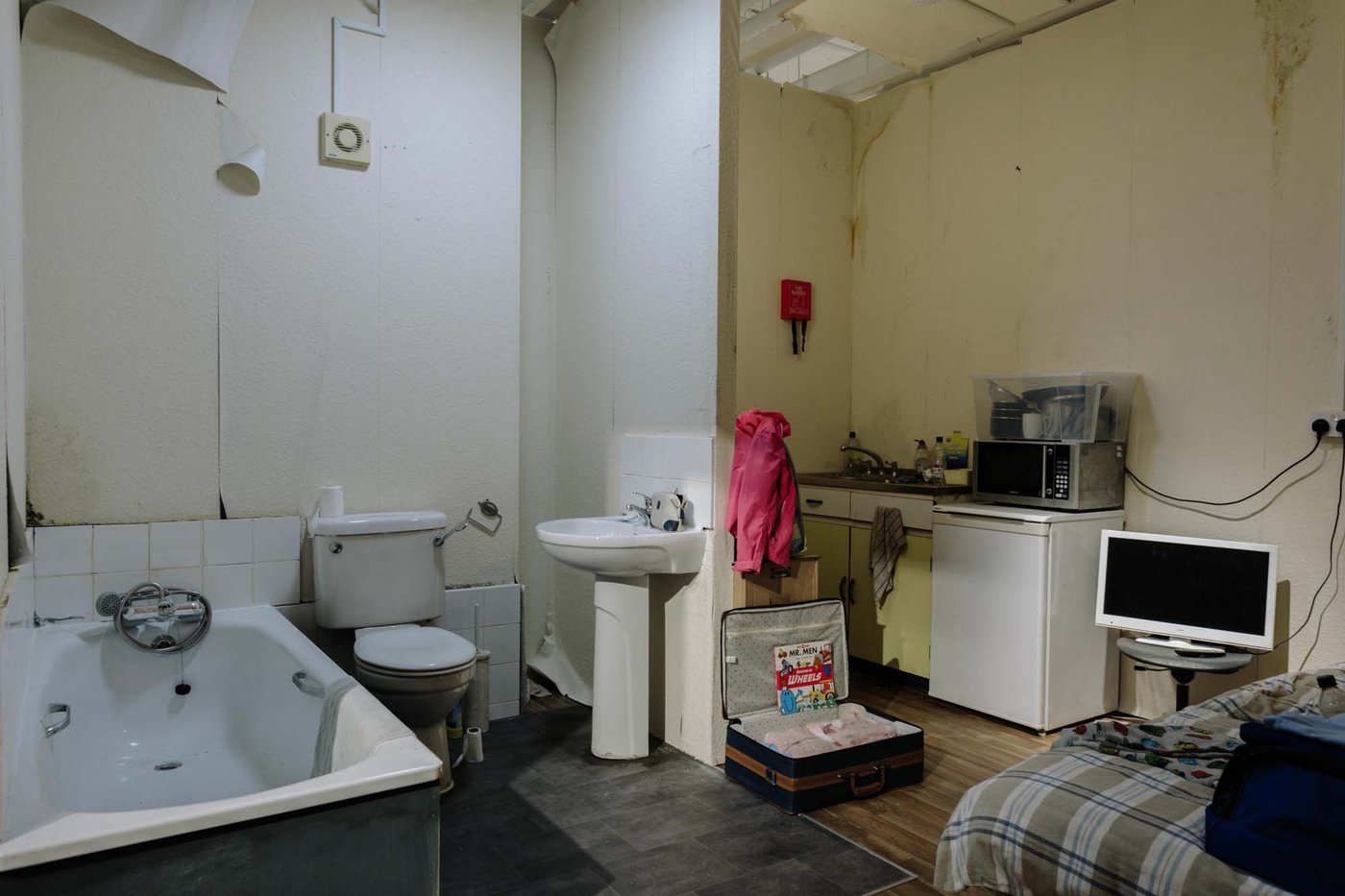 A dirty, cramped roomset with a bathroom, kitchenette and sleeping area.