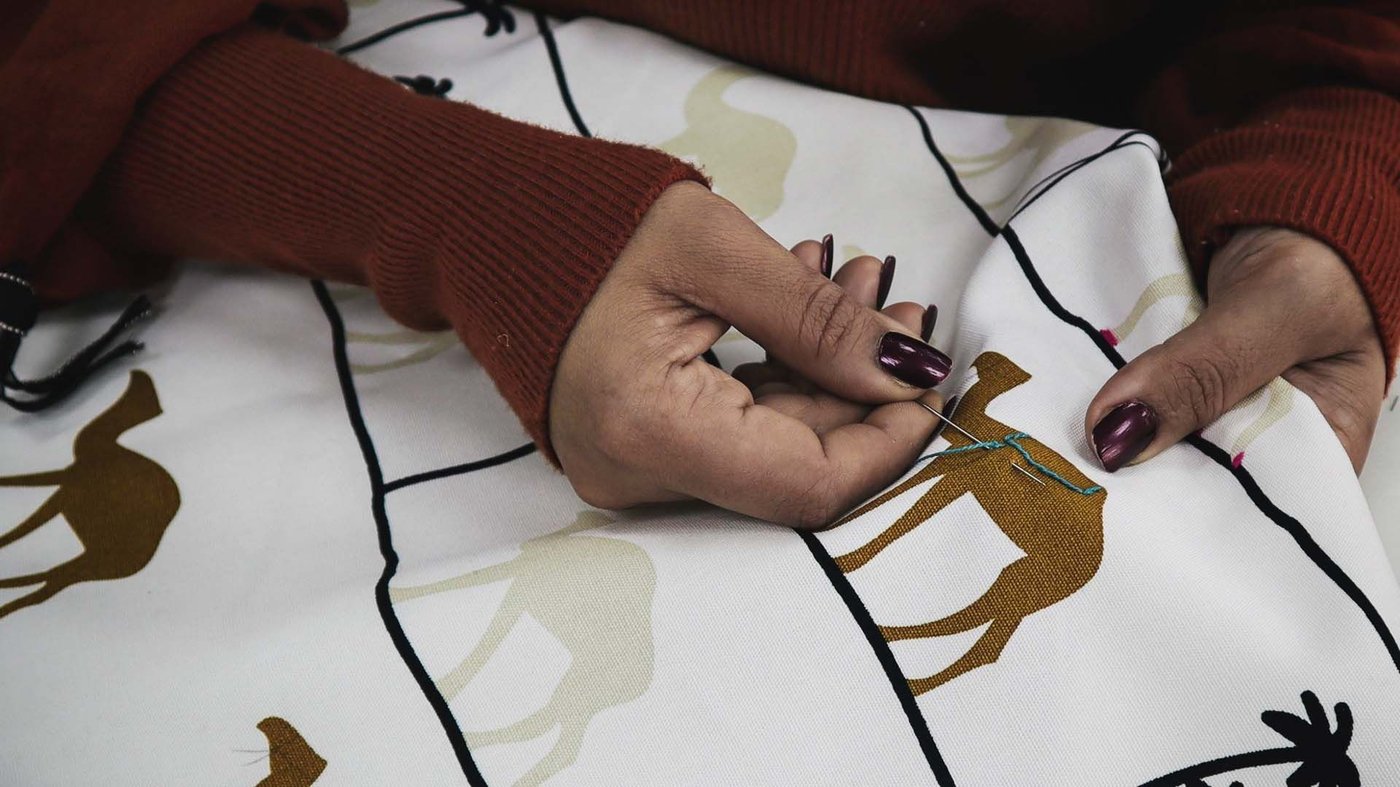 A pair of hands embroider a camel on a piece of fabric.