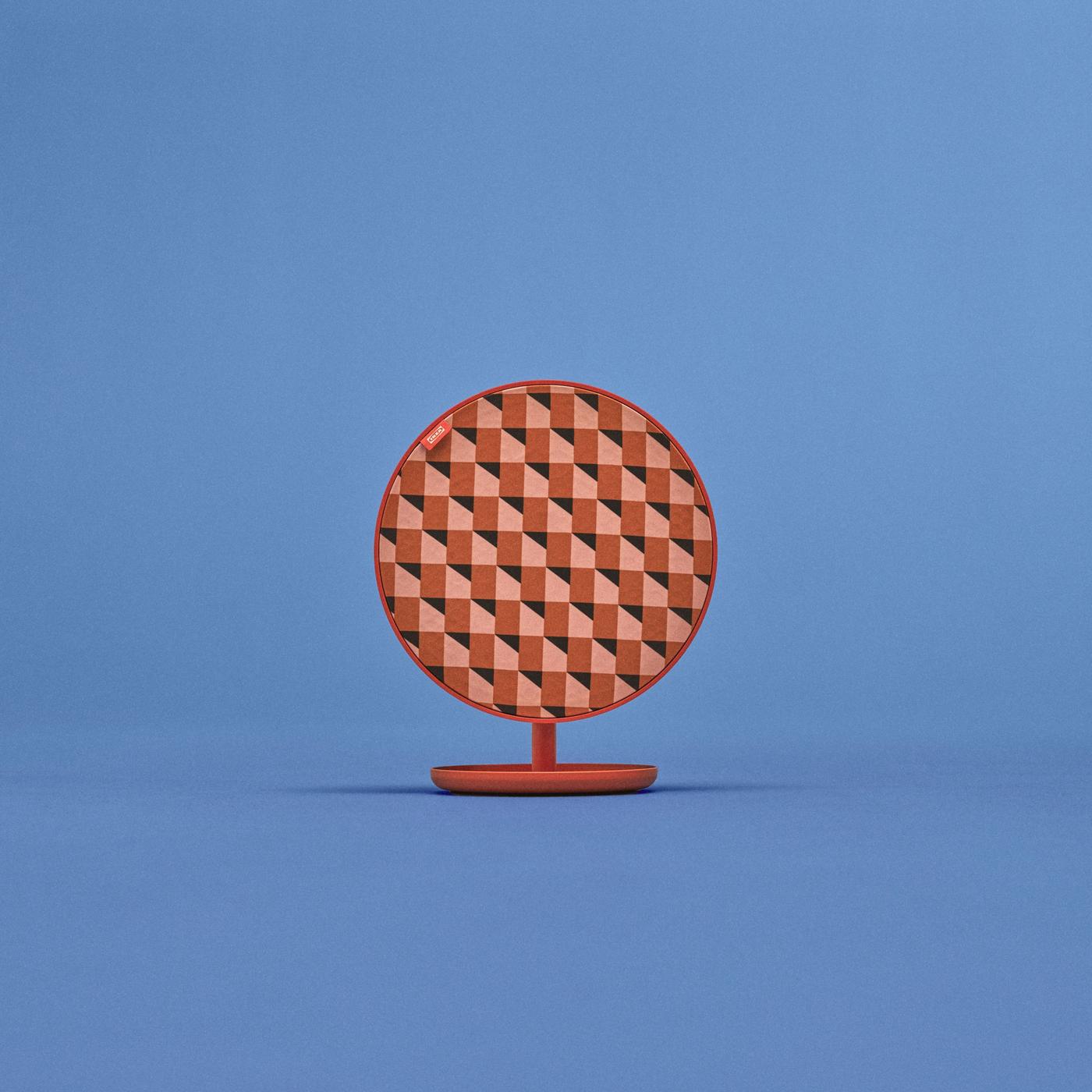 Round SOLSKYDD speaker on matching stand with red-pink zigzag pattern, set against a blue background.