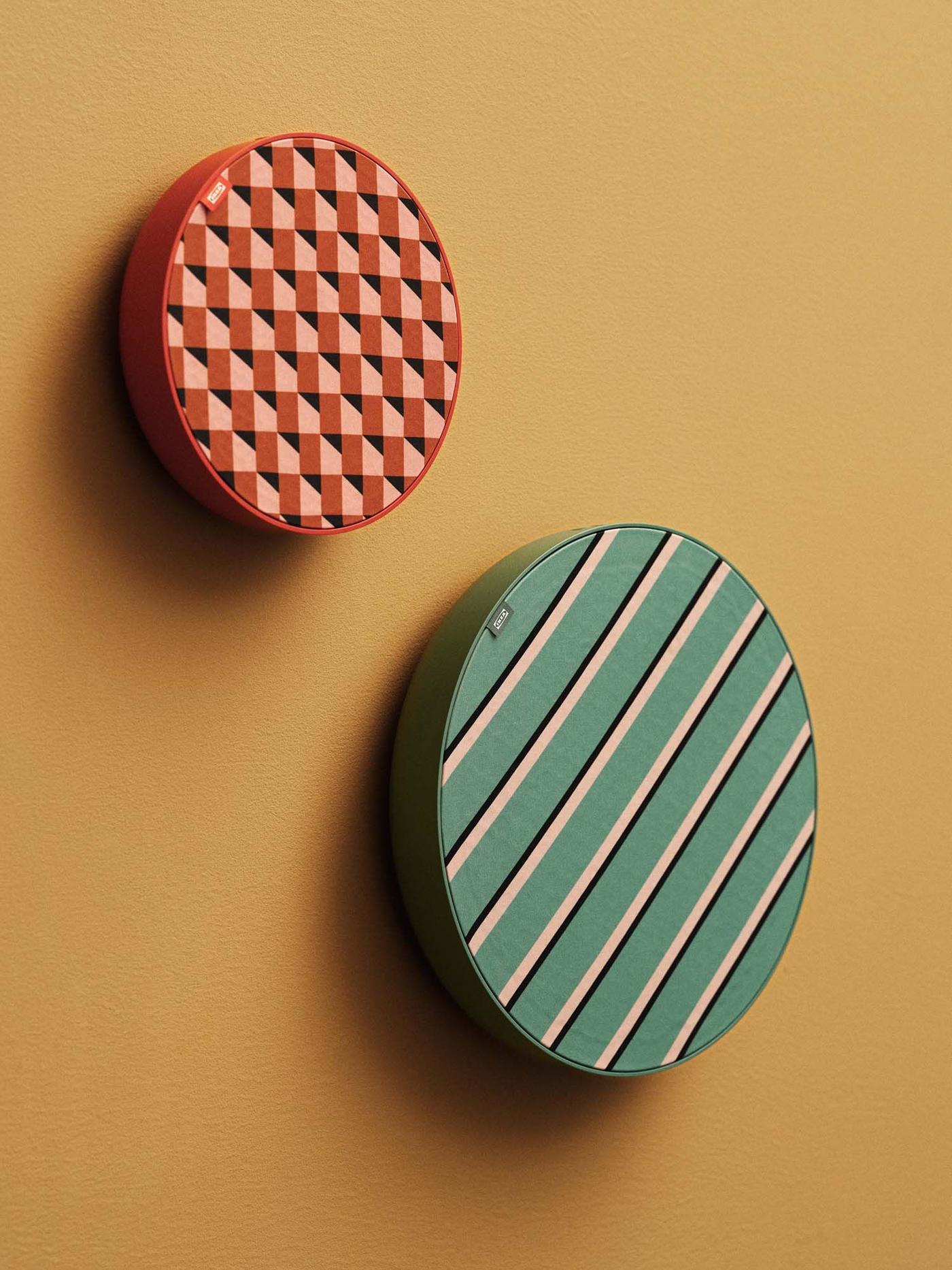 Two brightly coloured, patterned, round speakers hang on a mustard yellow coloured wall.