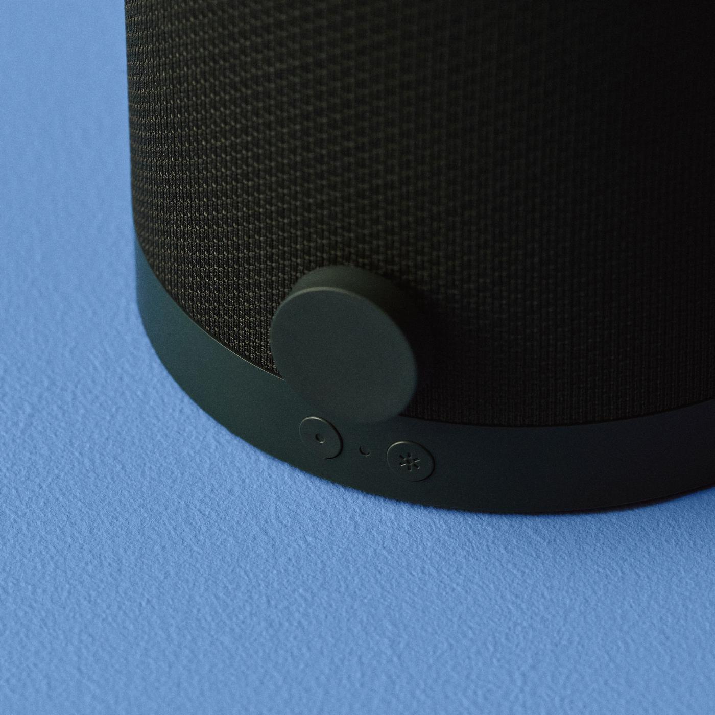 Close-up of a green KULGLASS table speaker, standing on a blue surface, showing side-angled view of green control buttons.