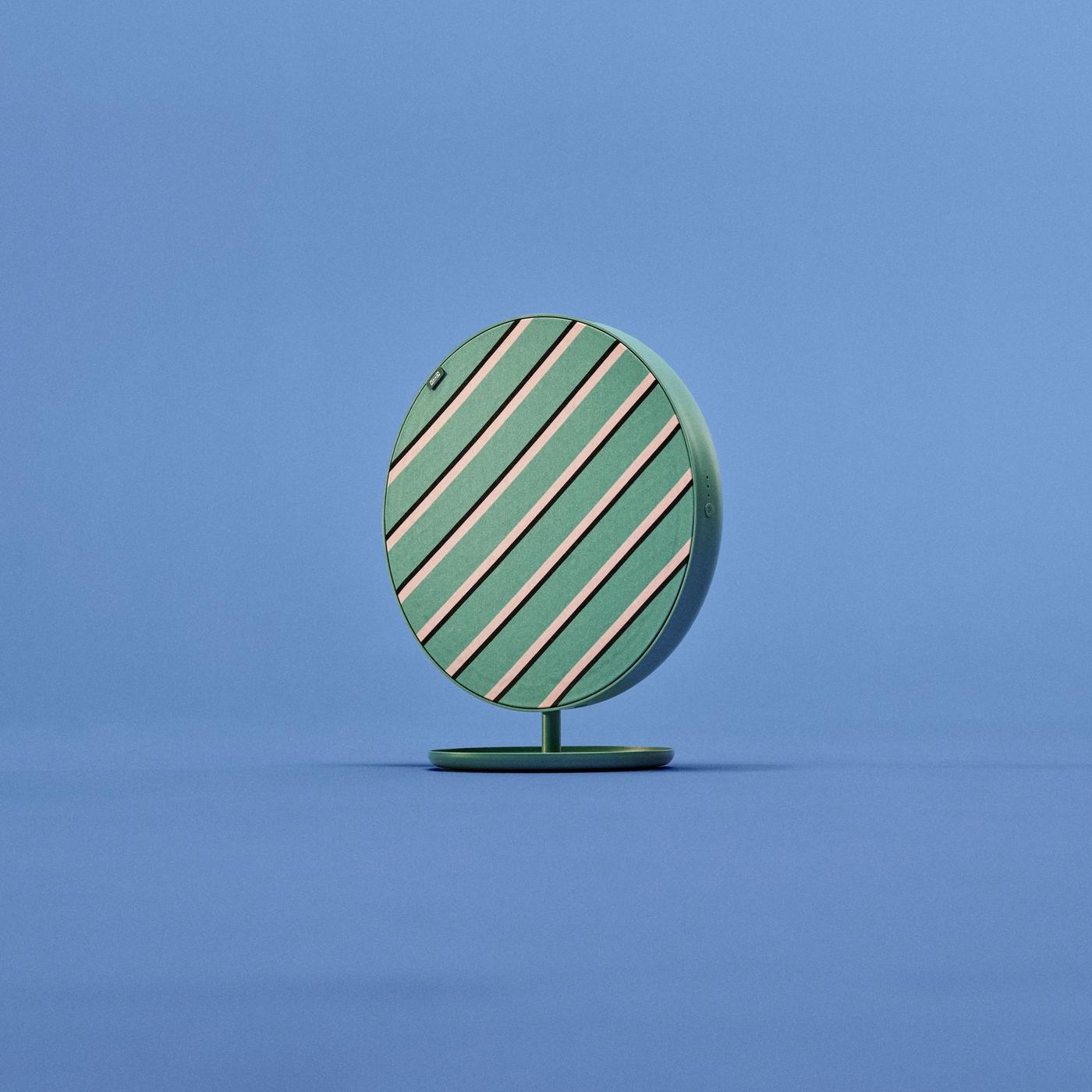 Side view of a medium-sized round SOLSKYDD speaker with green, beige, and black cross-striped pattern on a matching green stand, set against a blue background.