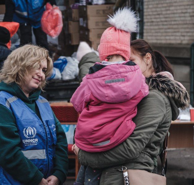 A woman holding a child in her arms, standing next to an aid worker fro UNHCR.