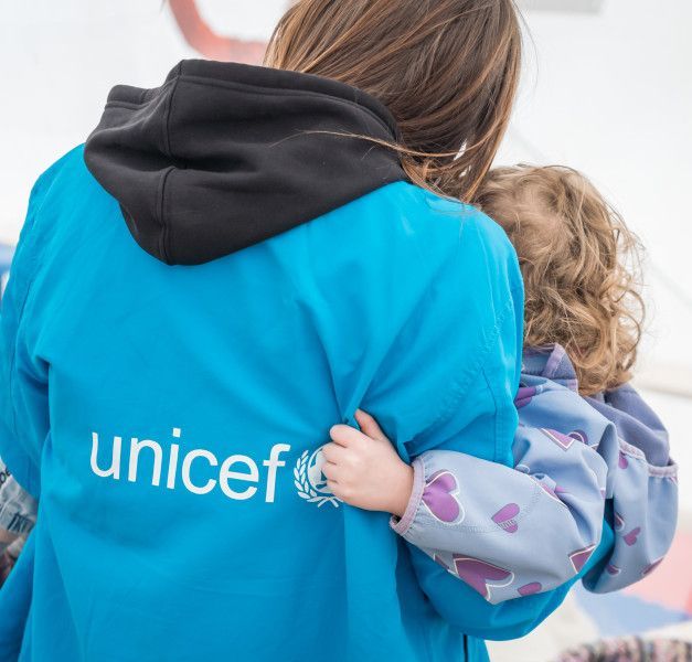 The back of a woman in a blue jacket carrying a child.