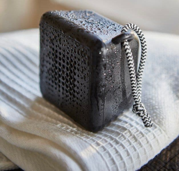 A black waterproof bluetooth speaker, covered with mist, standing on a white towel.