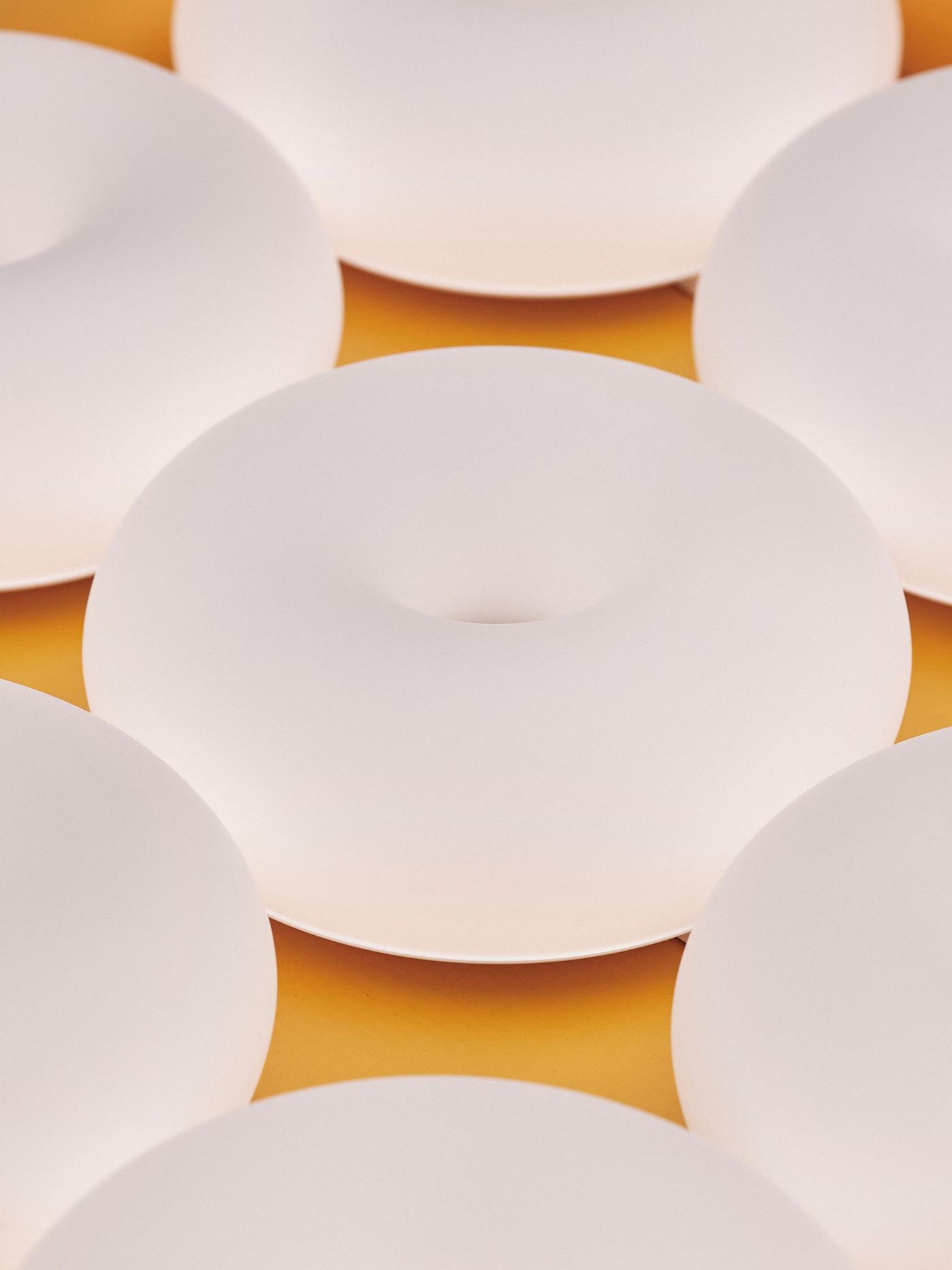 Donut-shaped lamps in a uniform white colour on a yellow surface, closely arranged.