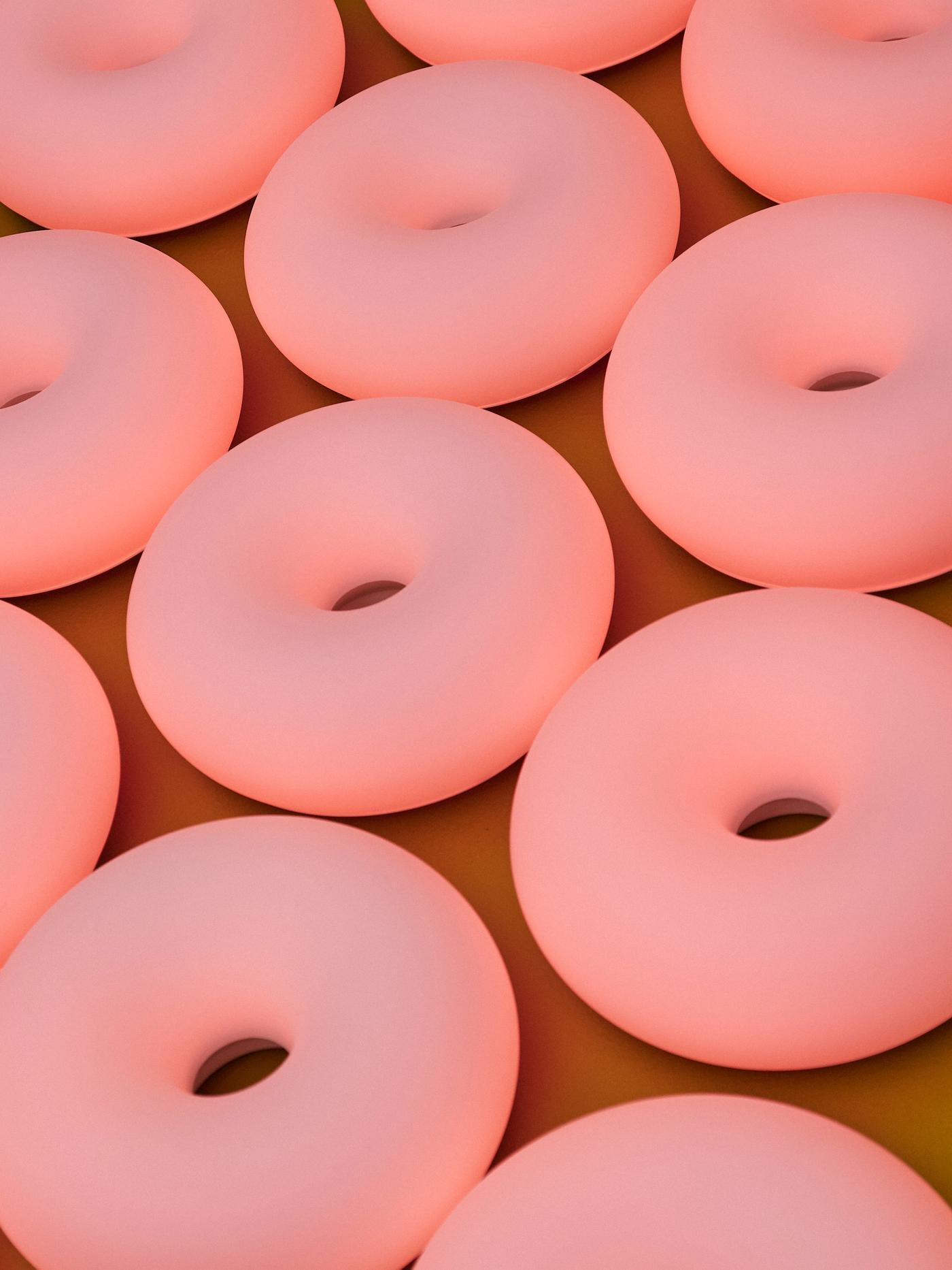 A close-up of multiple glowing pink donut-shaped lamps arranged in a grid-like pattern on a yellow surface.