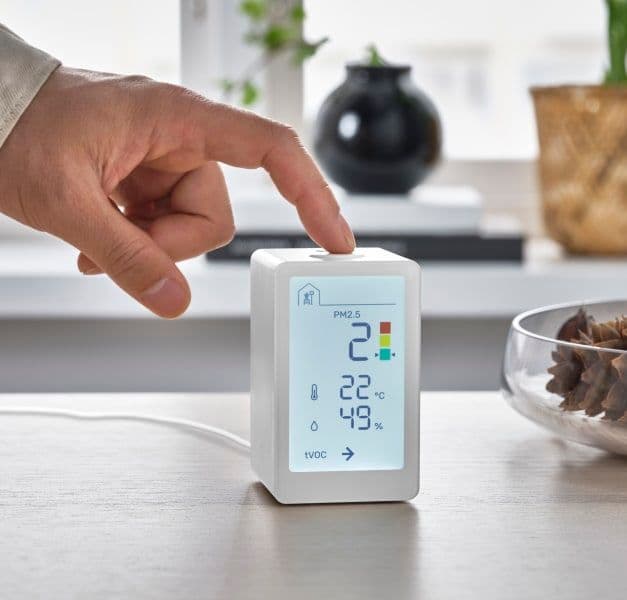 A finger pushing a button on a small white device displaying air quality.